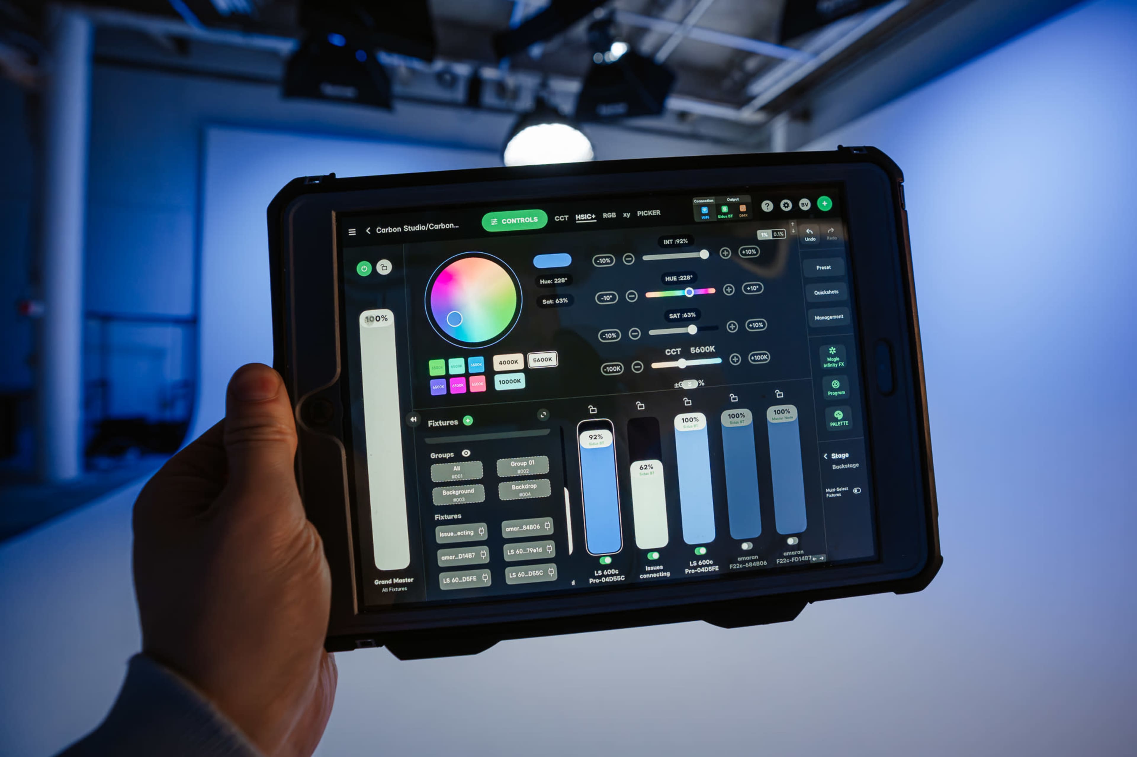 A person holds a tablet displaying a colorful control panel for lighting options in a studio setting.