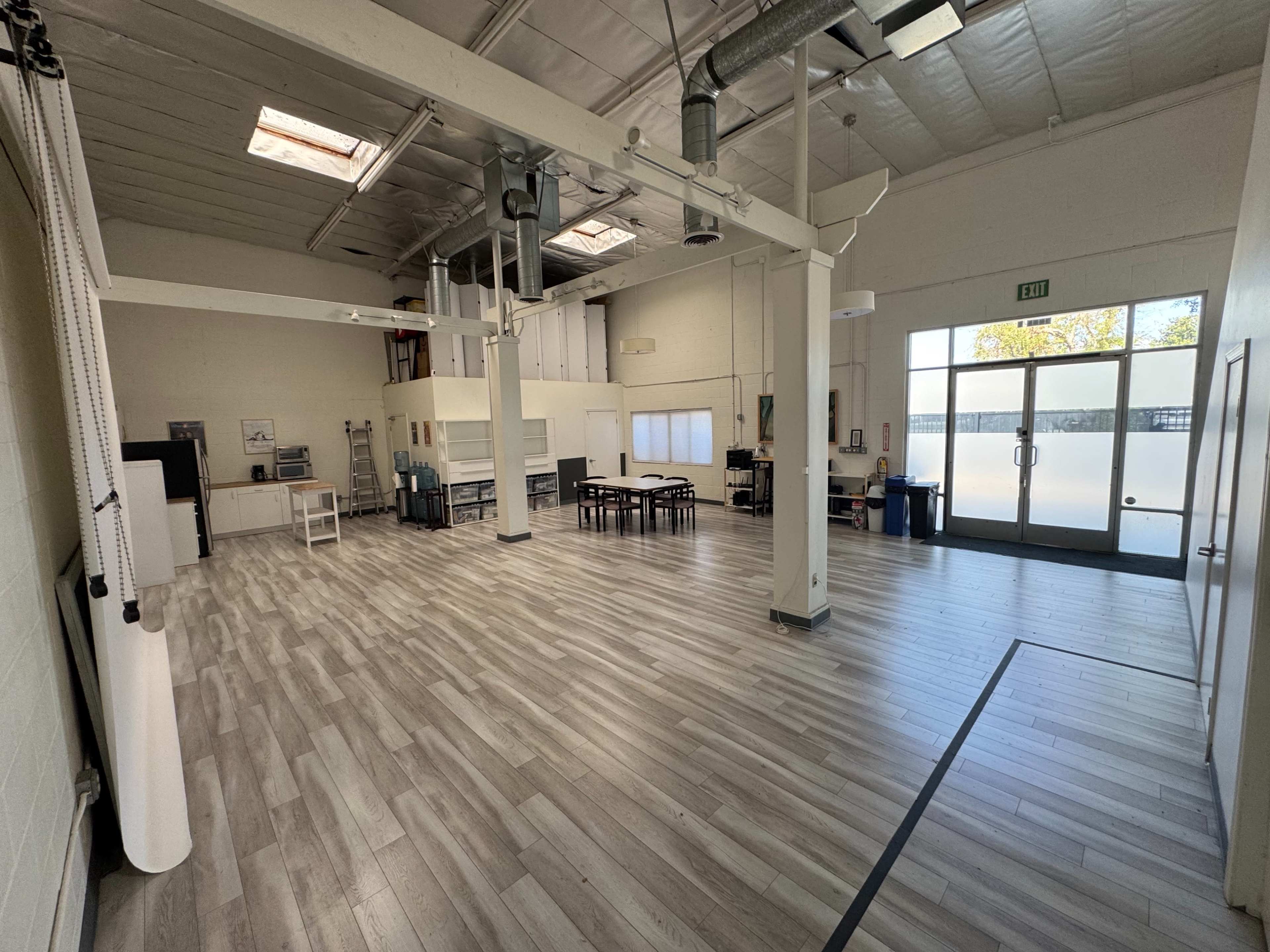 The image shows a spacious, well-lit indoor area featuring tables, chairs, and large windows.