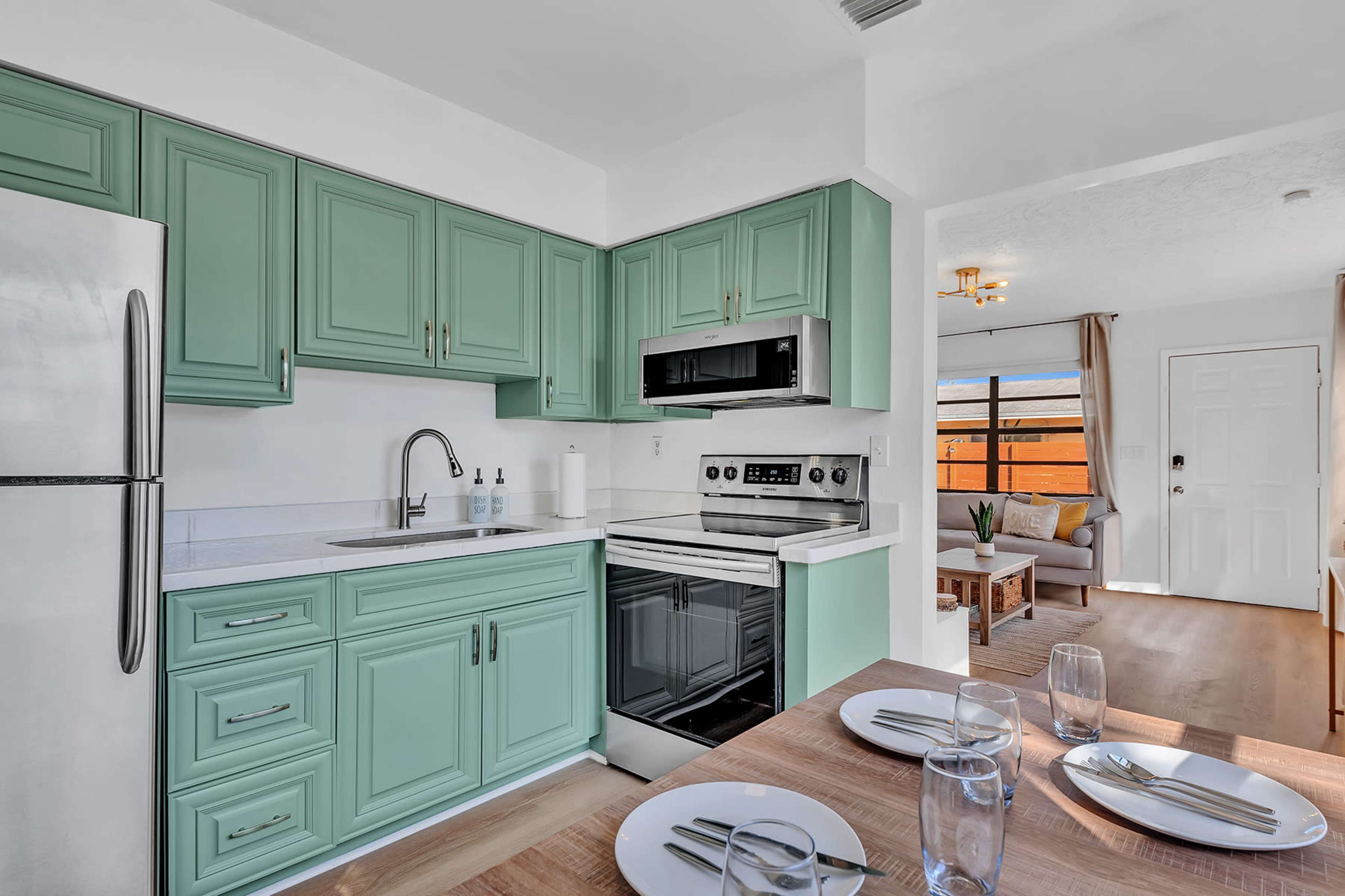 A modern kitchen with mint green cabinets and stainless steel appliances, adjacent to a dining area with a table set for four.