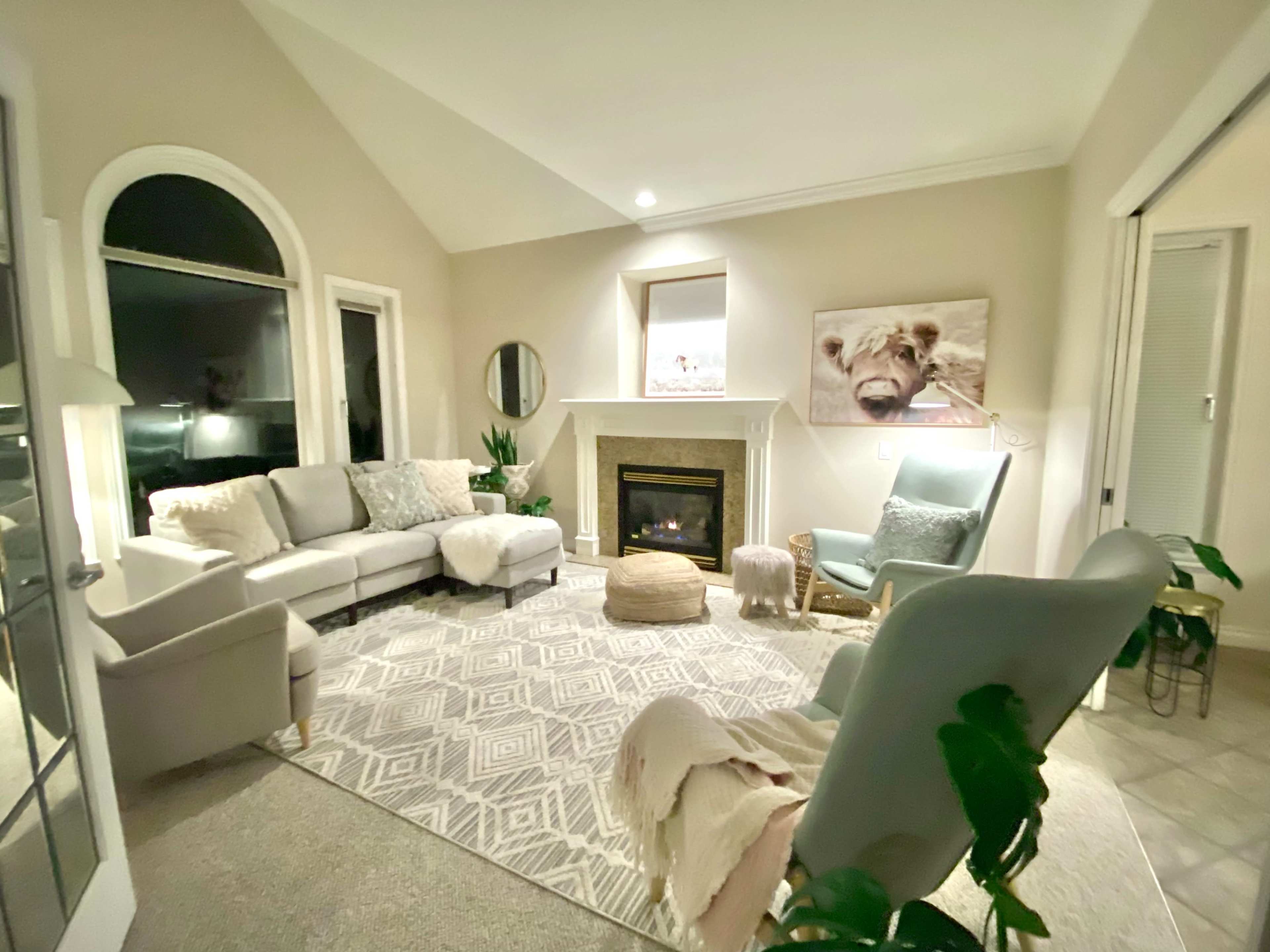 A cozy living room with a fireplace, a large area rug, and comfortable seating arrangements, including a light gray sofa and a green armchair.