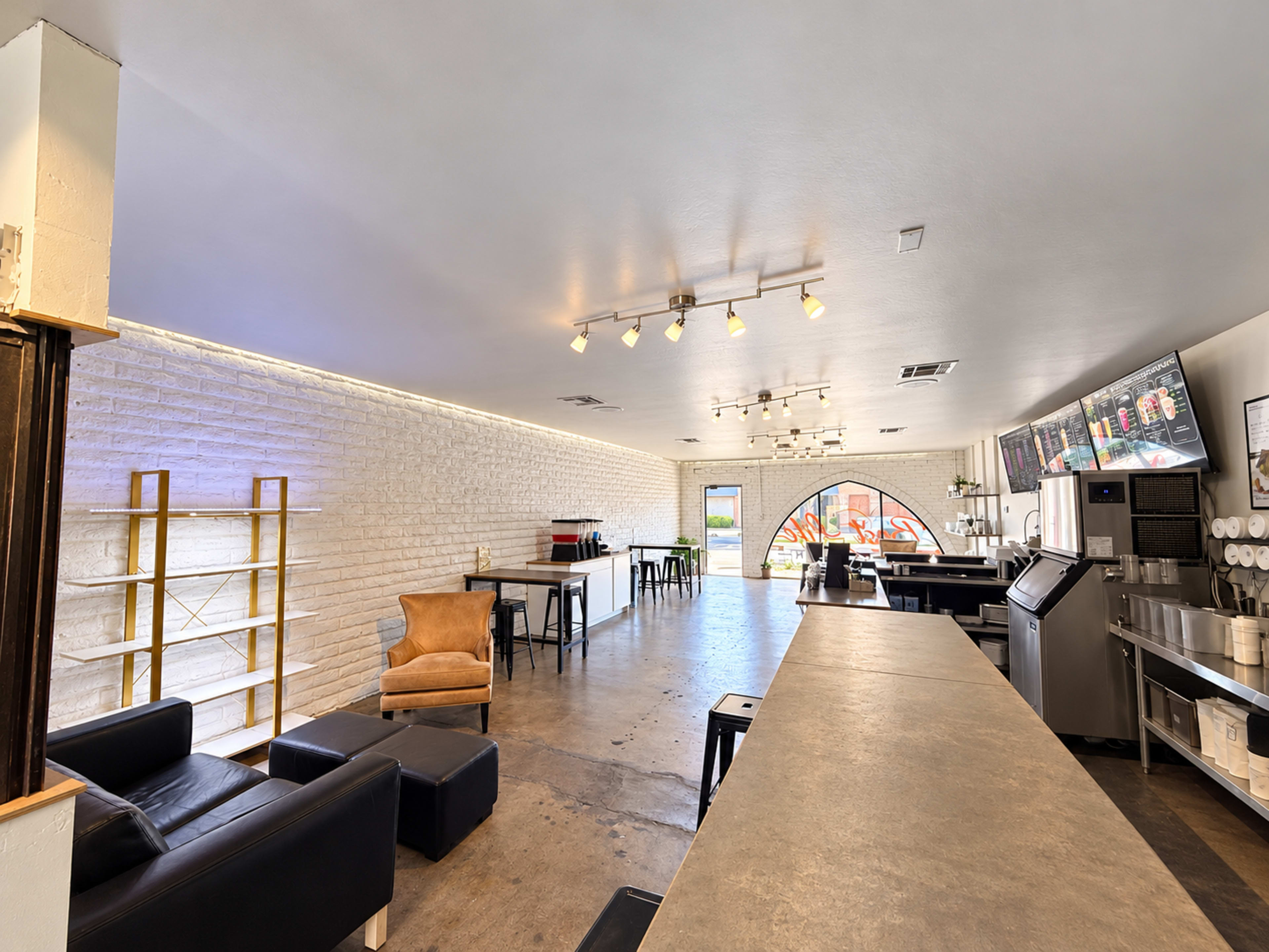 The image shows a spacious interior of a cafe featuring a long counter, tables, and a large arched window with natural light illuminating the space.
