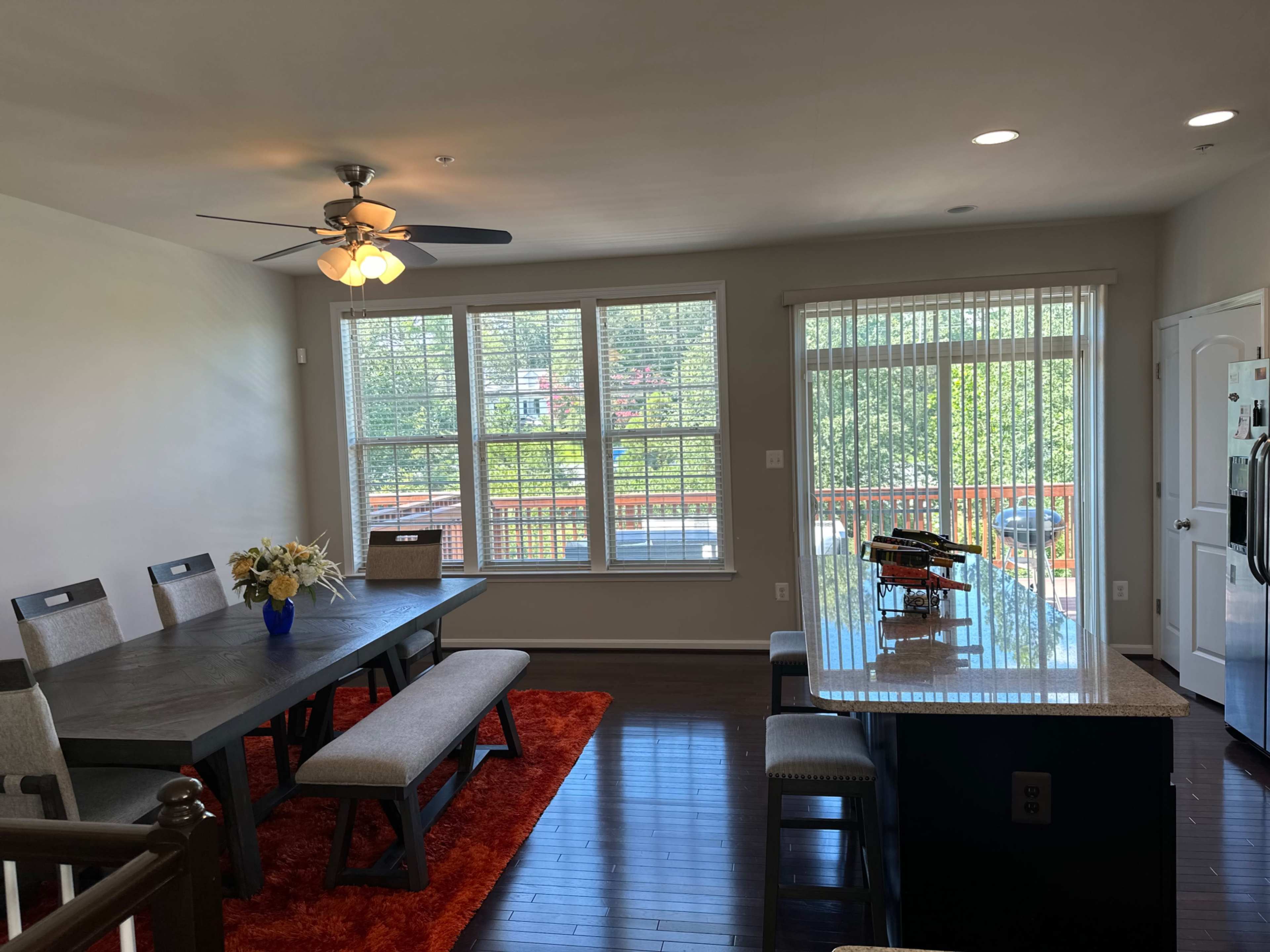 A dining area features a table with seating for eight, adjacent to a kitchen island, with large windows allowing natural light to fill the space.