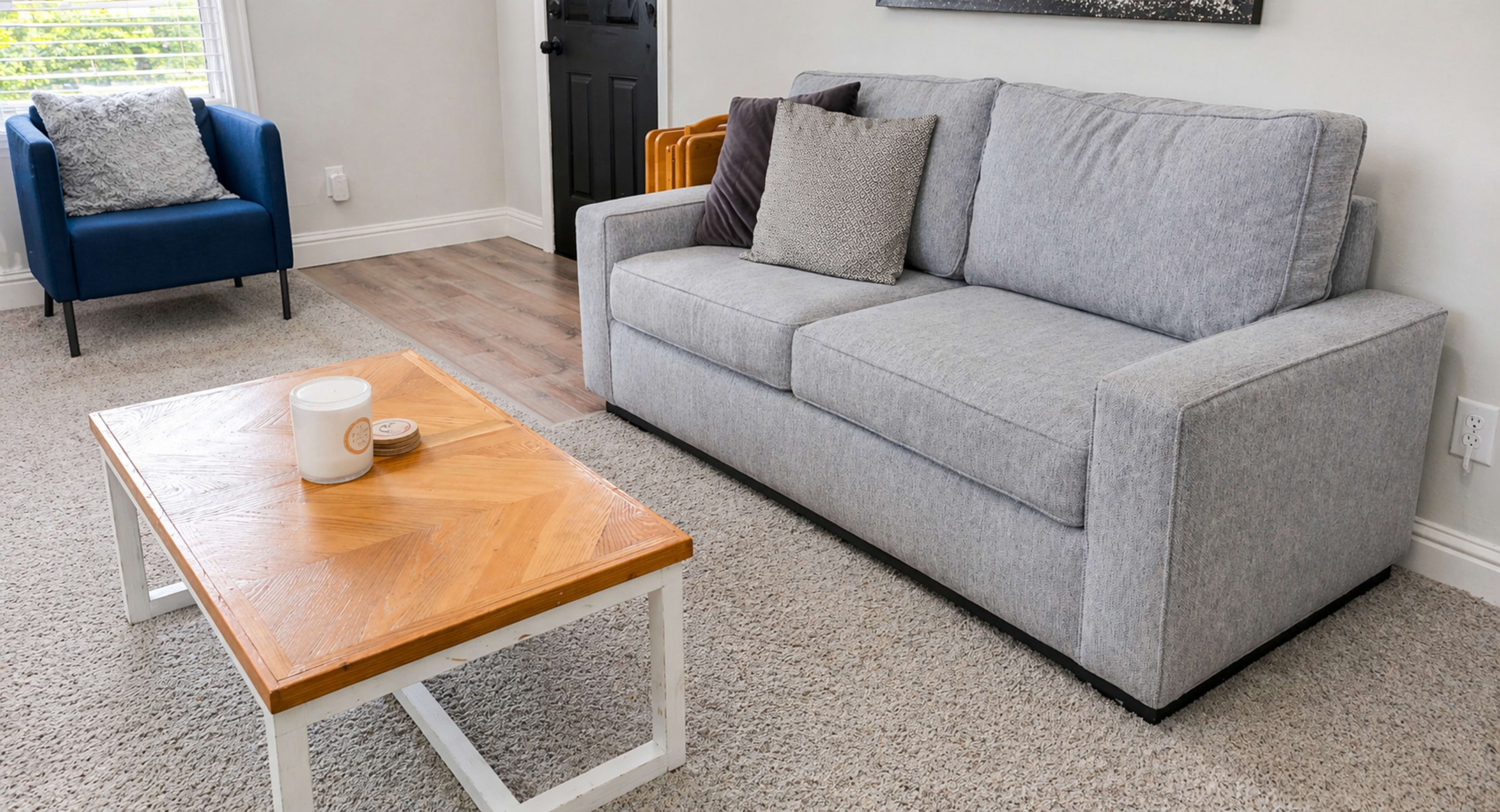 The image shows a modern living room featuring a gray sofa, a wooden coffee table with a herringbone pattern, and a blue armchair.