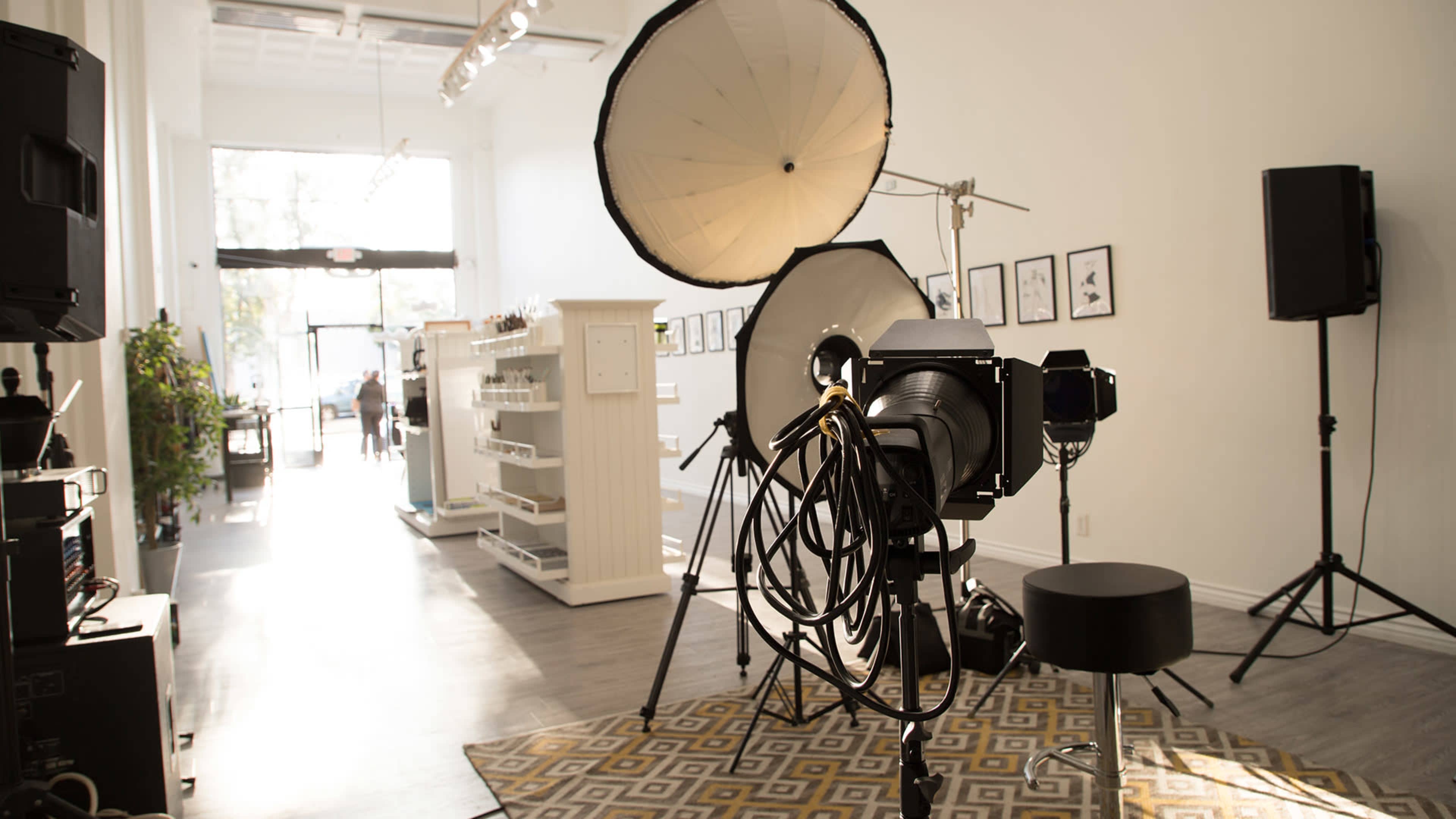 A photography studio setup with large light sources, a camera on a tripod, and a patterned rug on the floor.