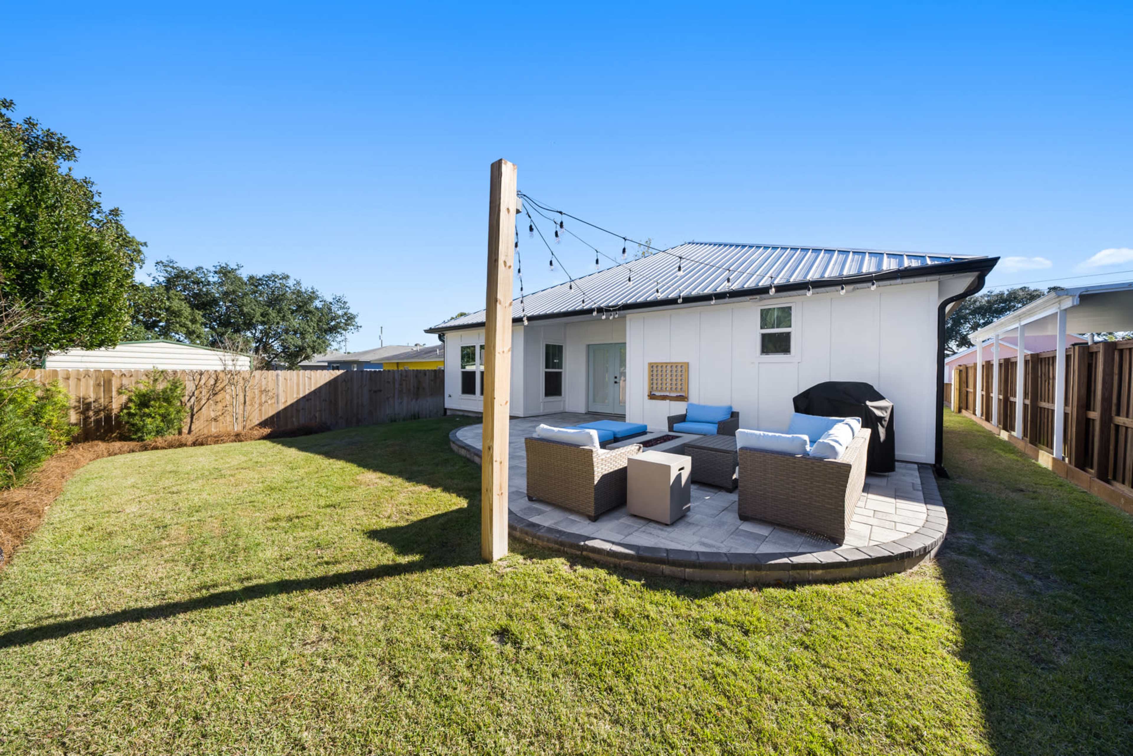 A backyard features a circular patio with seating and a grill beside a house with a metal roof.