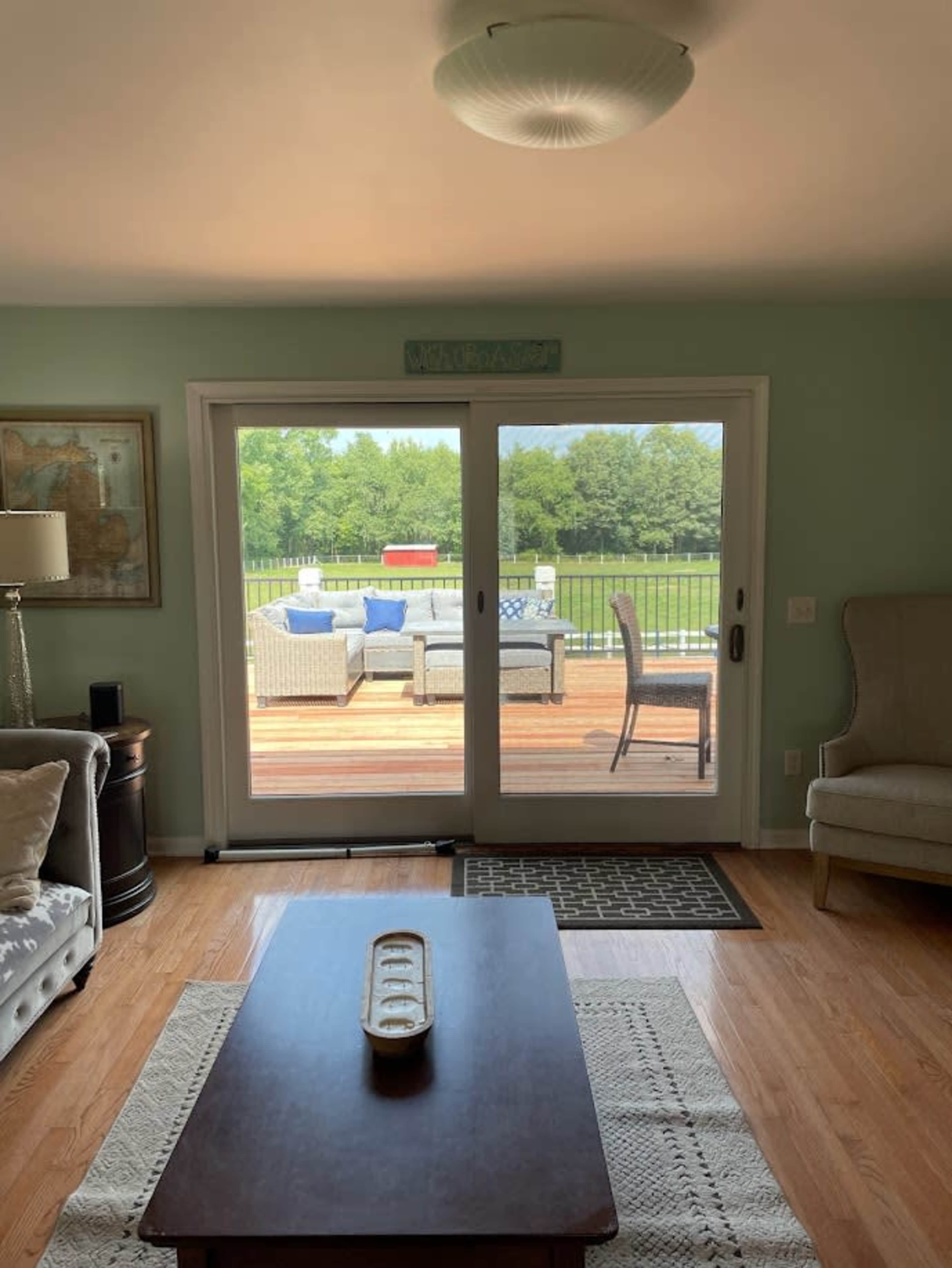 A living room with a sofa and an armchair overlooks a patio with outdoor furniture and a grassy area beyond.
