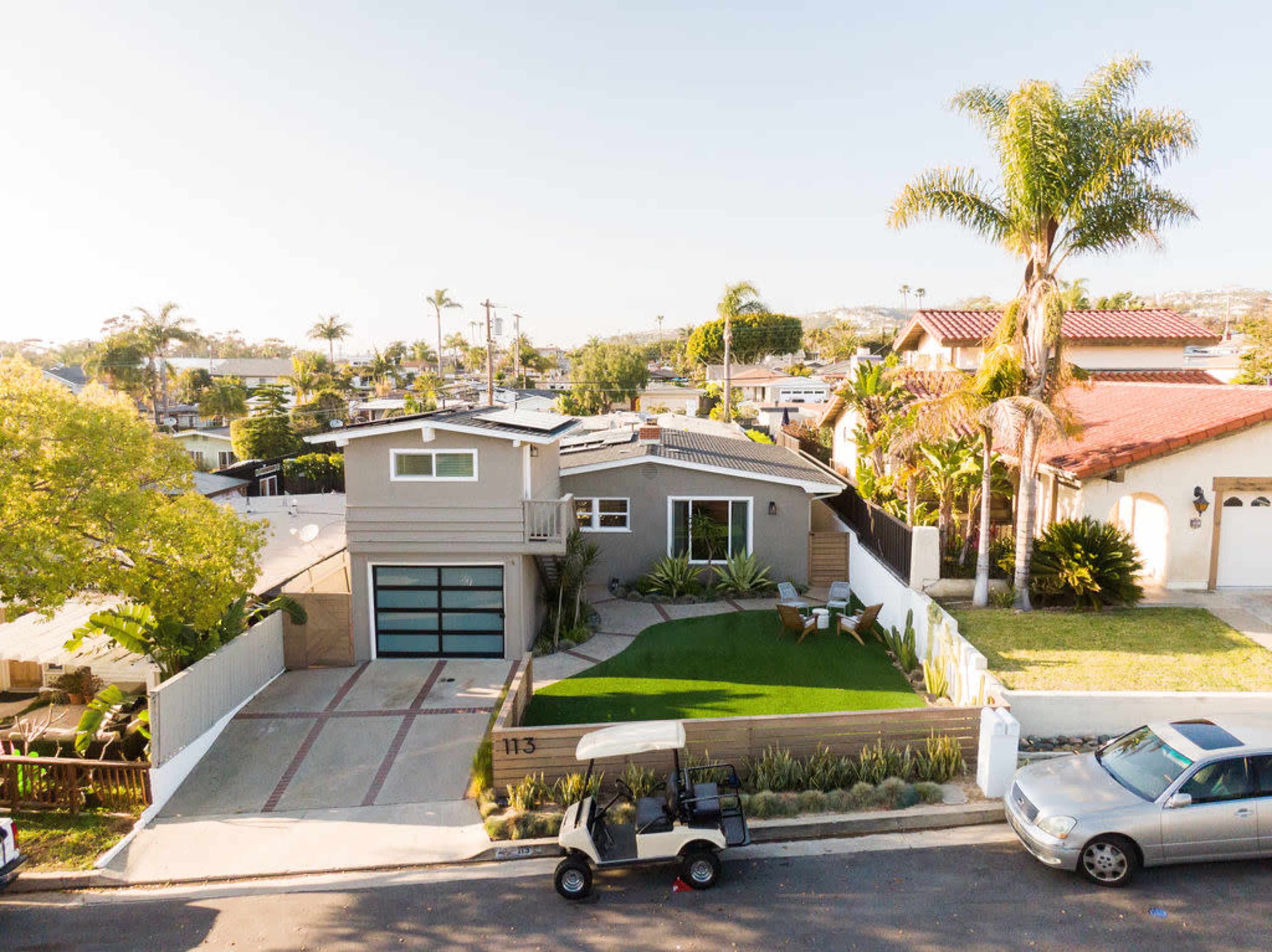 A two-story gray house with a landscaped front yard, a driveway, and a golf cart parked on the street.