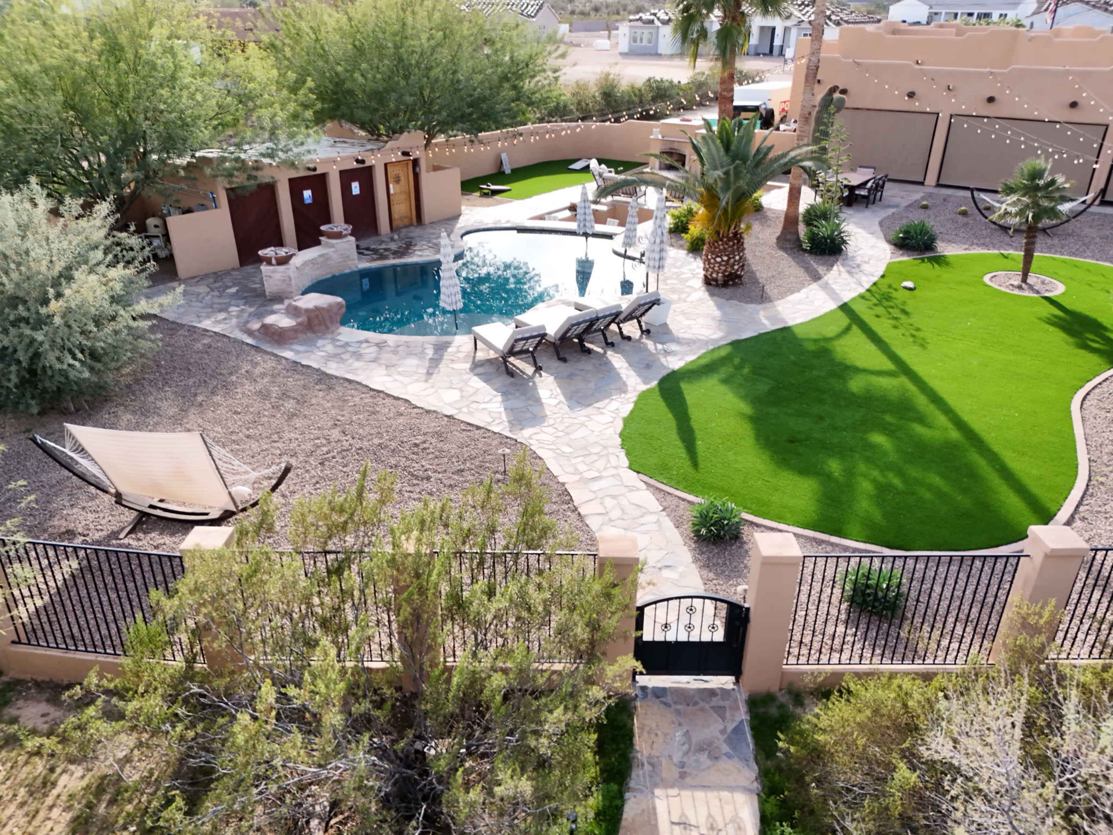 The image shows a landscaped backyard with a swimming pool, lounge chairs, and a hammock surrounded by greenery and decorative stones.