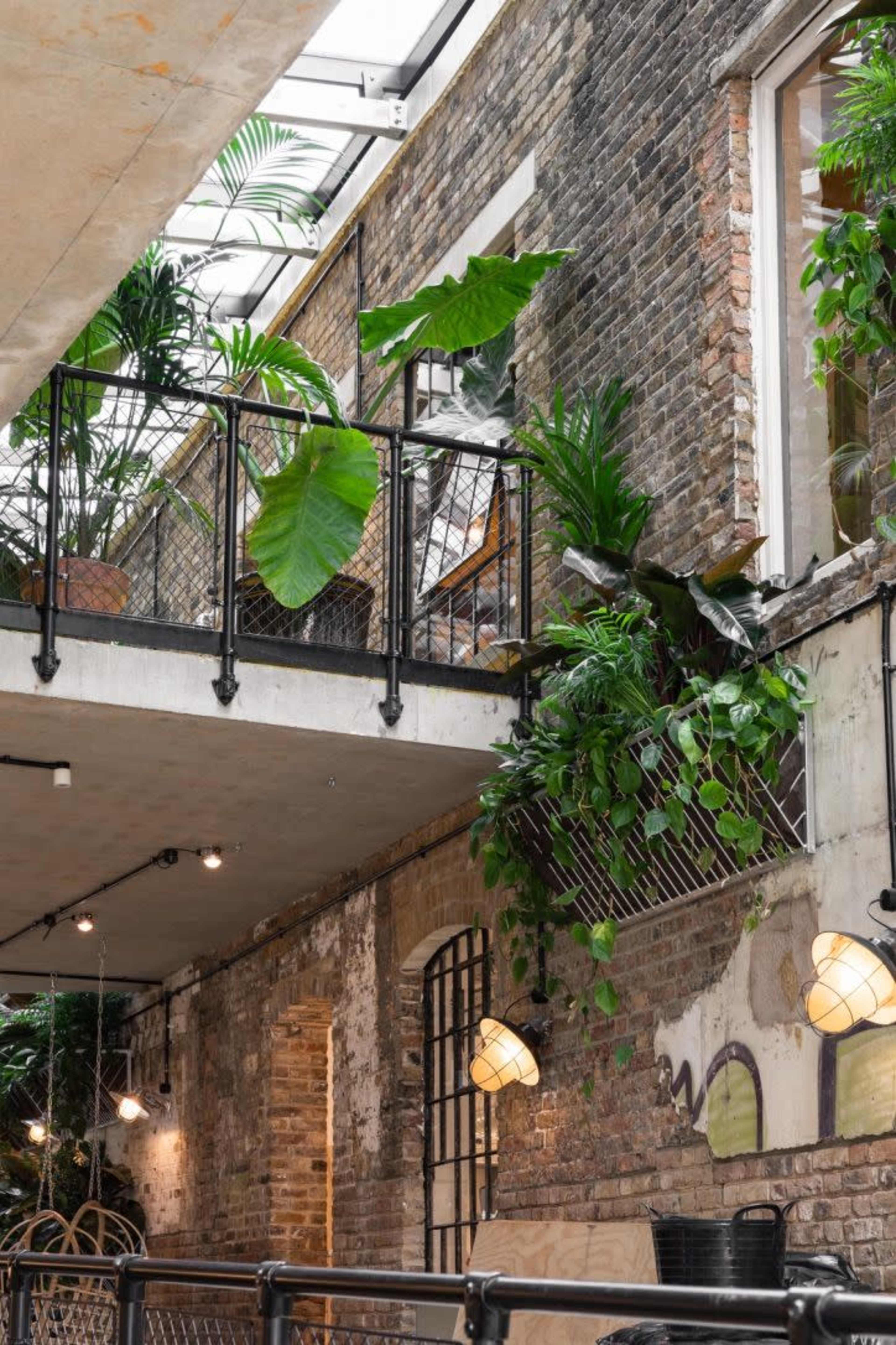 An indoor space featuring a balcony with potted plants alongside a brick wall and industrial-style light fixtures.