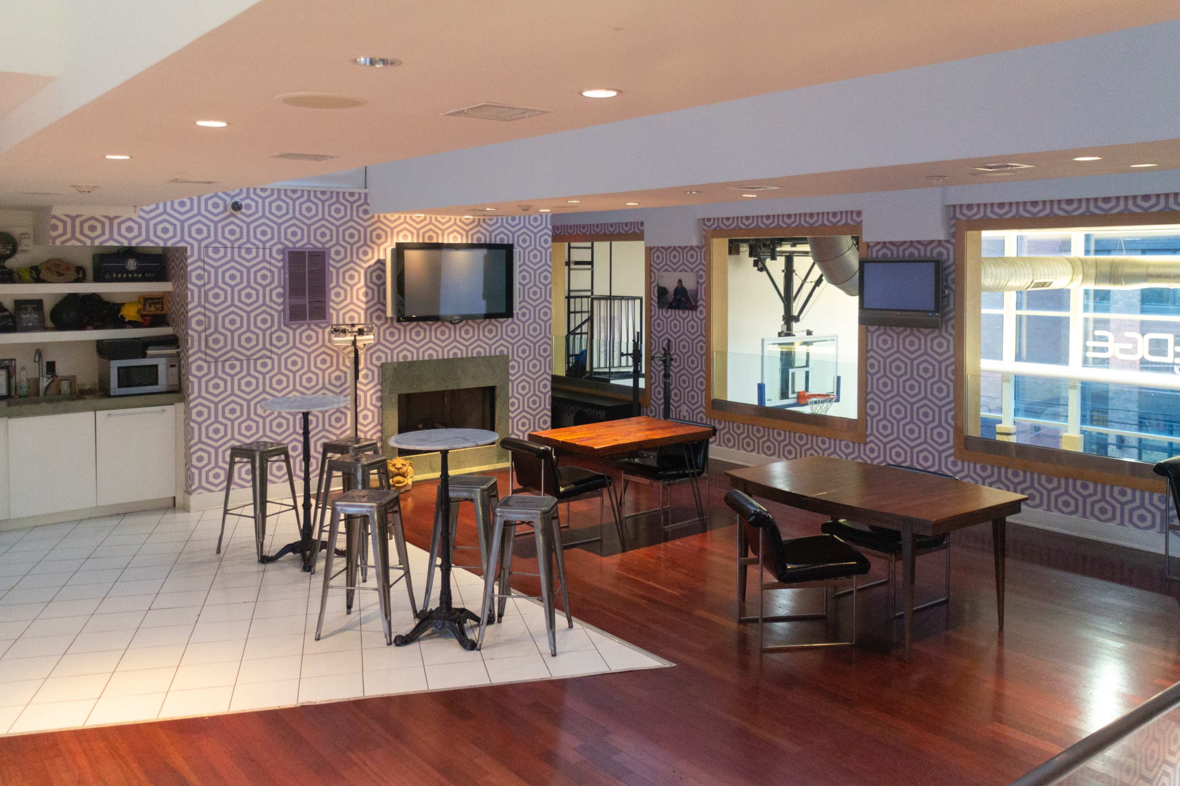 A modern open-concept lounge area featuring a kitchen with appliances, multiple tables with chairs, and distinctive patterned wallpaper.