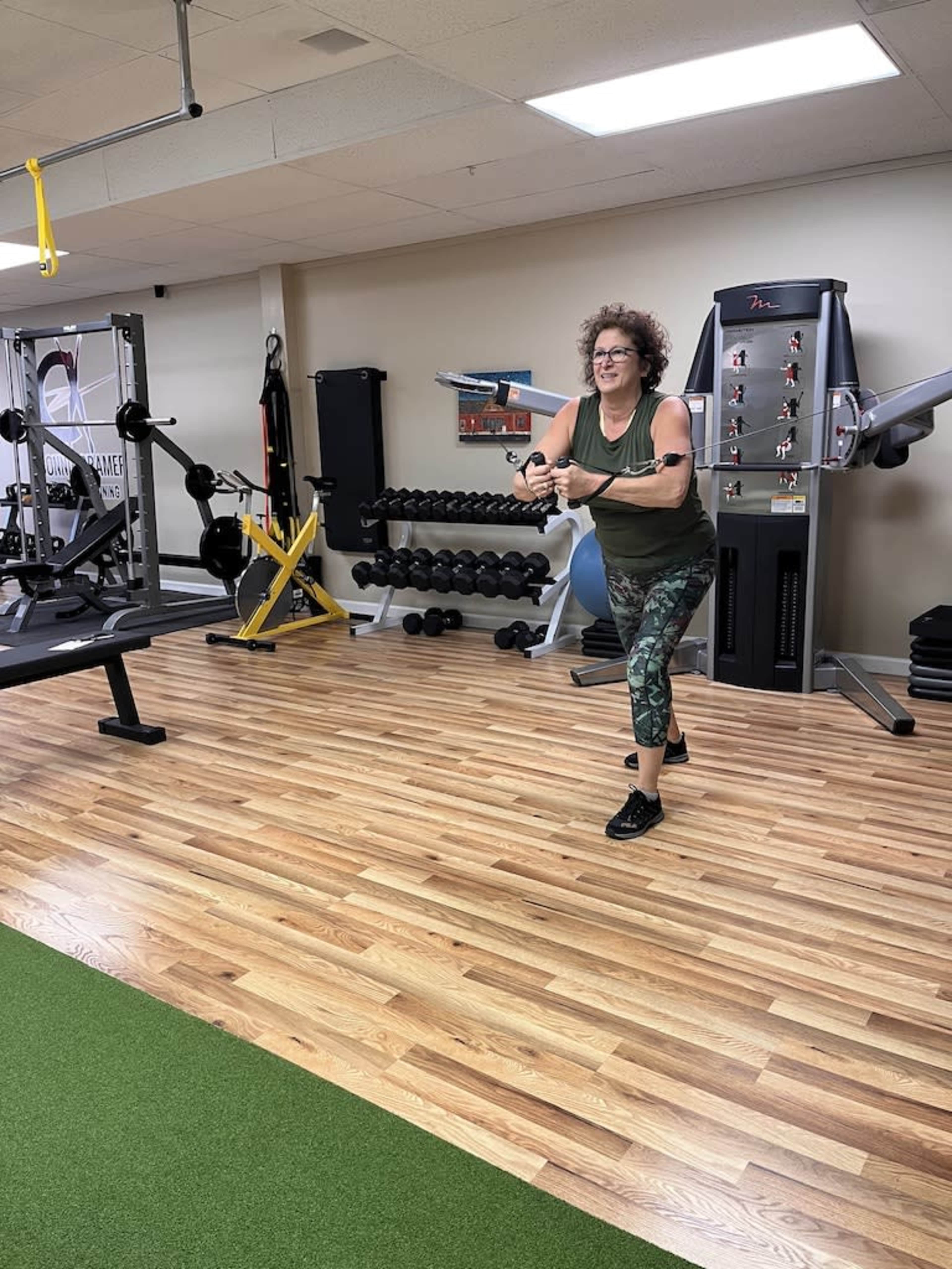 A woman in workout attire performs an exercise with a resistance band in a gym setting.
