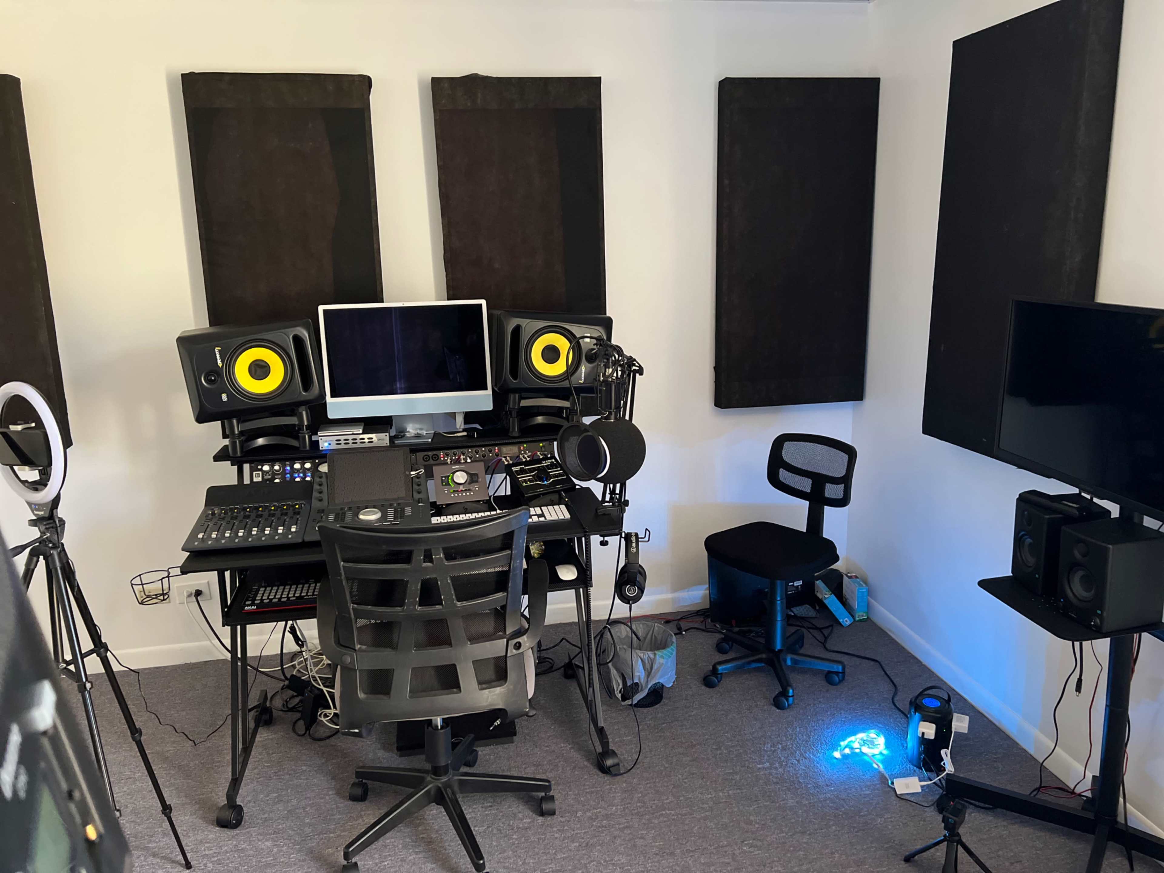 A music studio is equipped with soundproof panels, a computer, audio mixing equipment, and microphones.