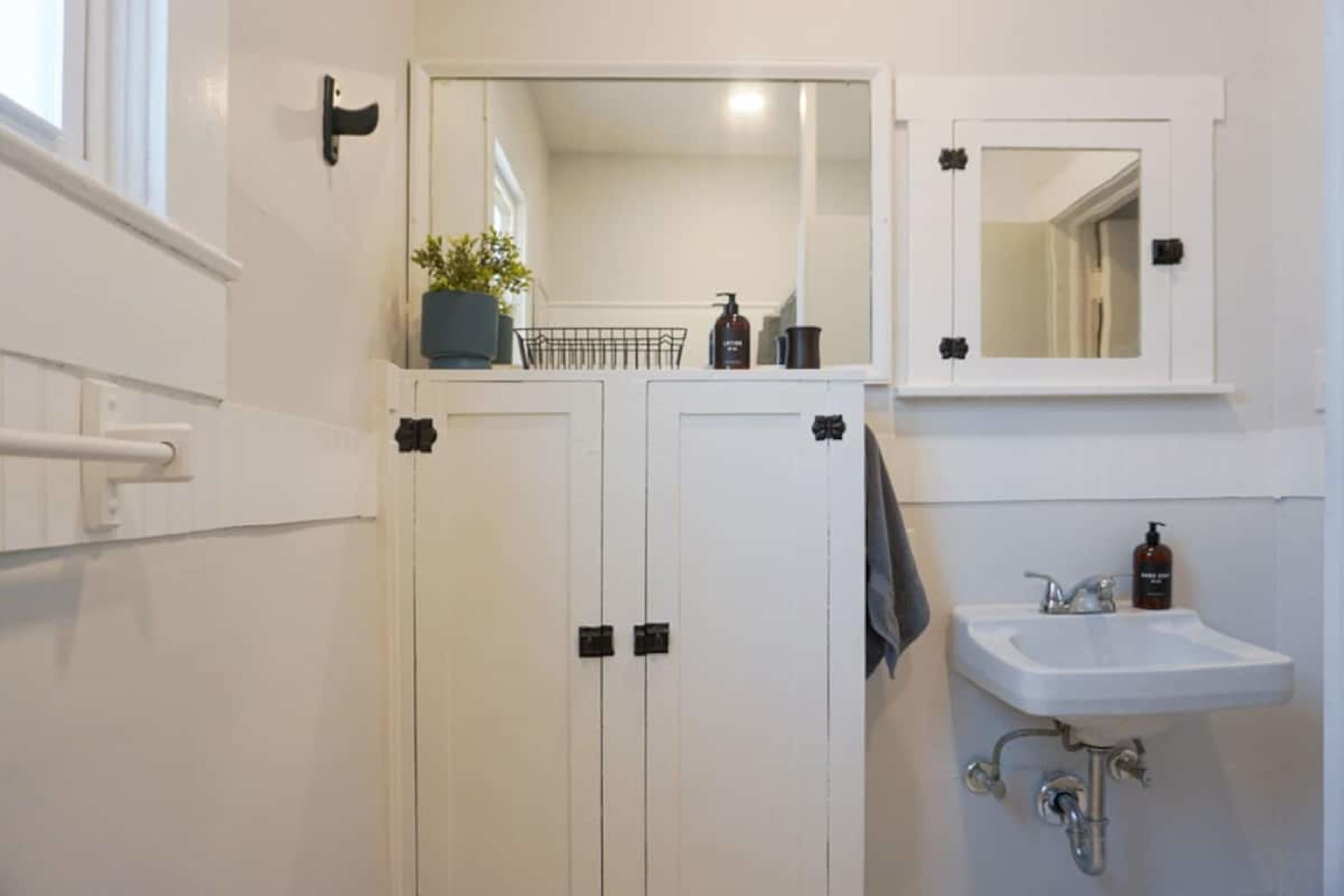 A small, tidy bathroom with white cabinets, a sink, and mirrors on the walls.