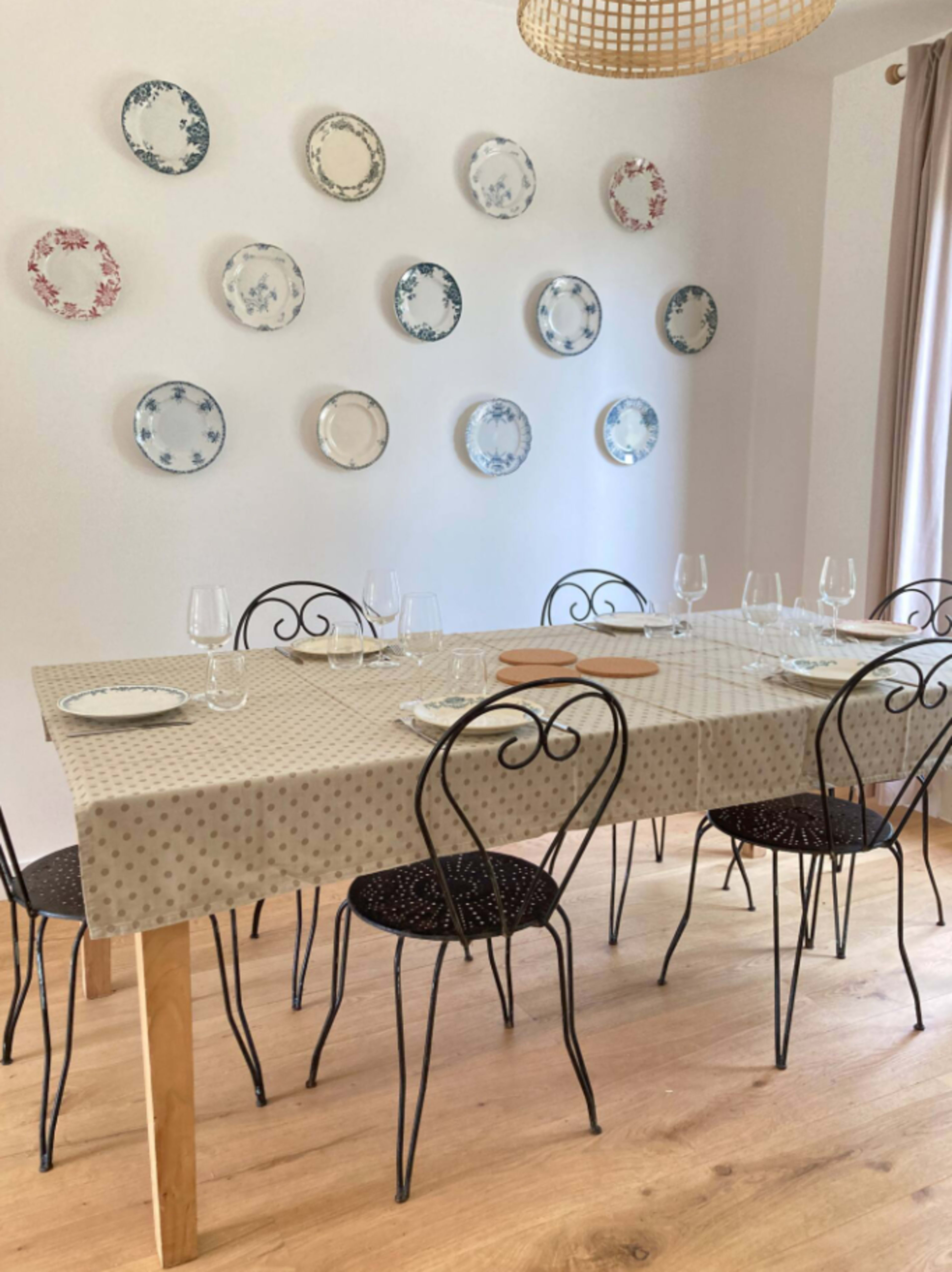 A dining table set with plates and glassware is surrounded by black metal chairs, with decorative plates arranged on the wall above.