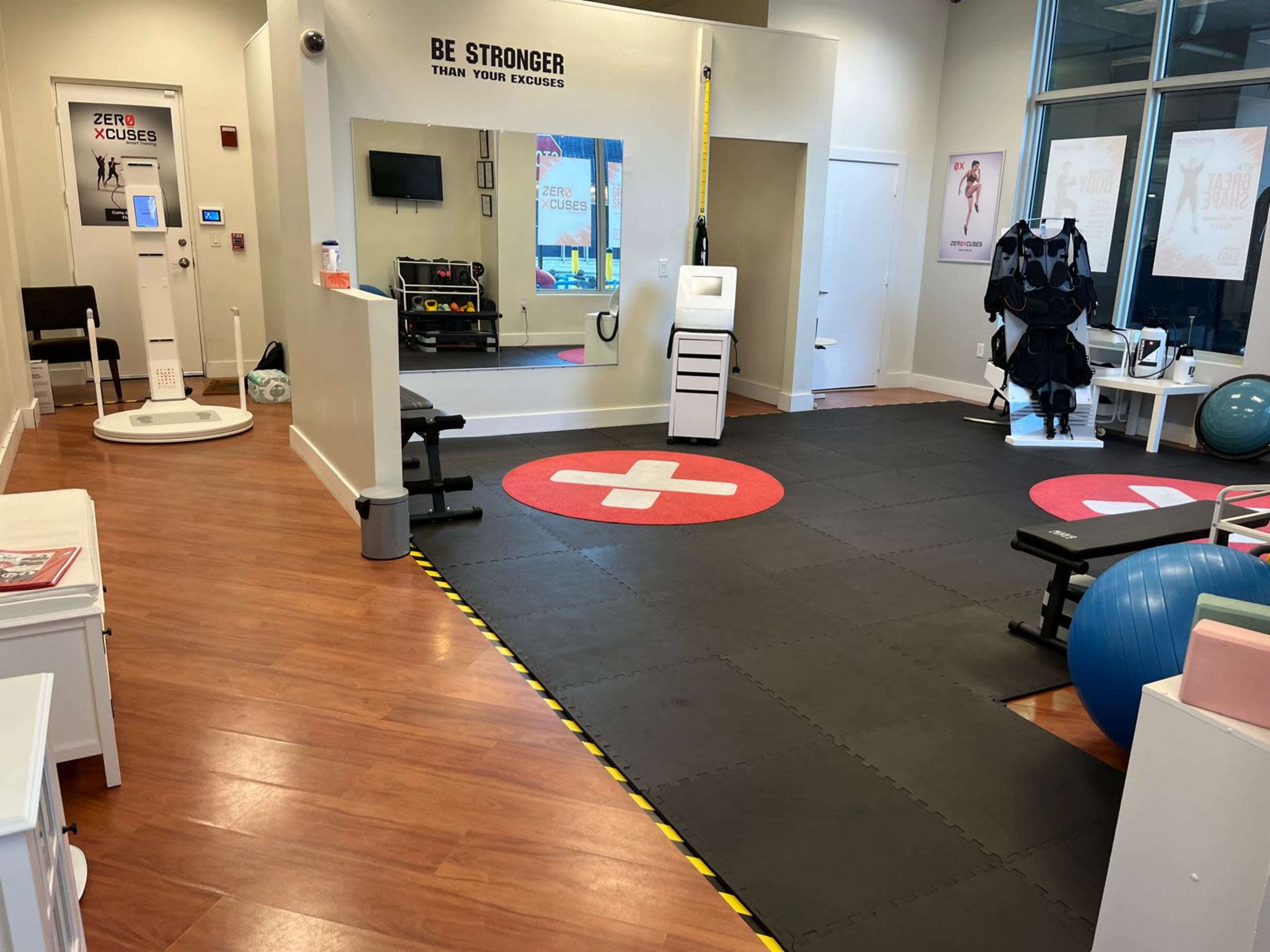The image shows a modern fitness studio with exercise equipment, mats on the floor, and motivational signage on the walls.
