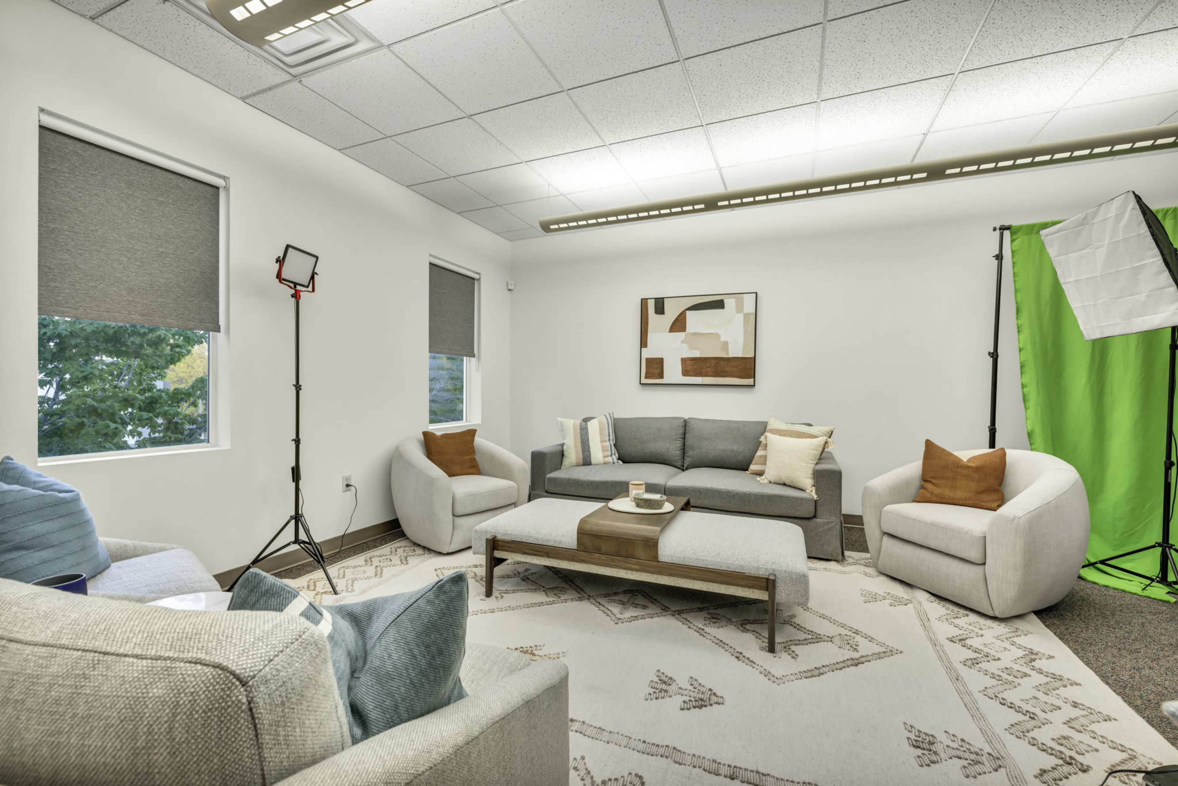 A modern office lounge with gray sofas, a coffee table, and a green screen backdrop set up in one corner.