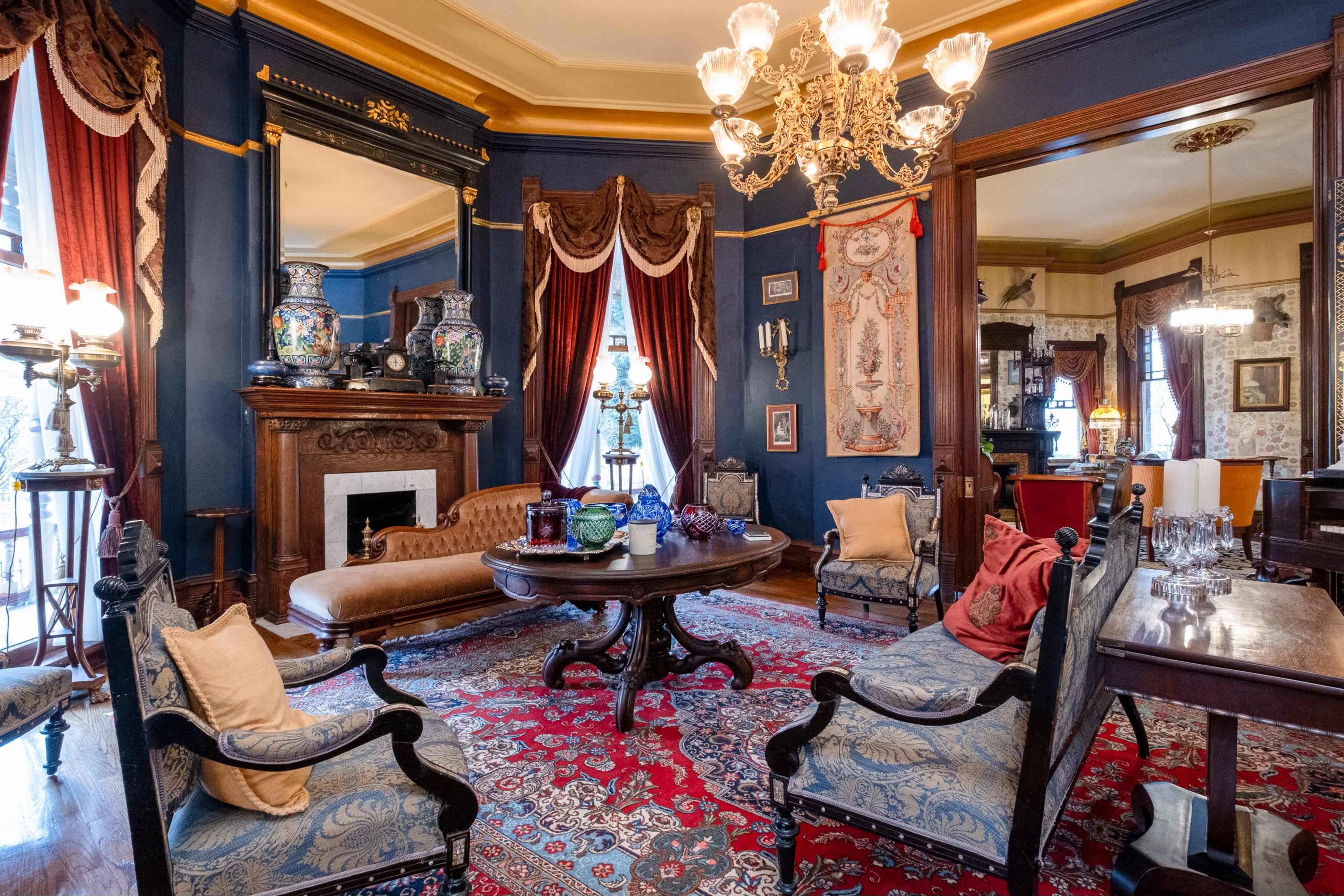 The image depicts a richly decorated parlor featuring a vintage sofa, ornate chandelier, and intricate rugs, surrounded by elegant furnishings and wall decor.