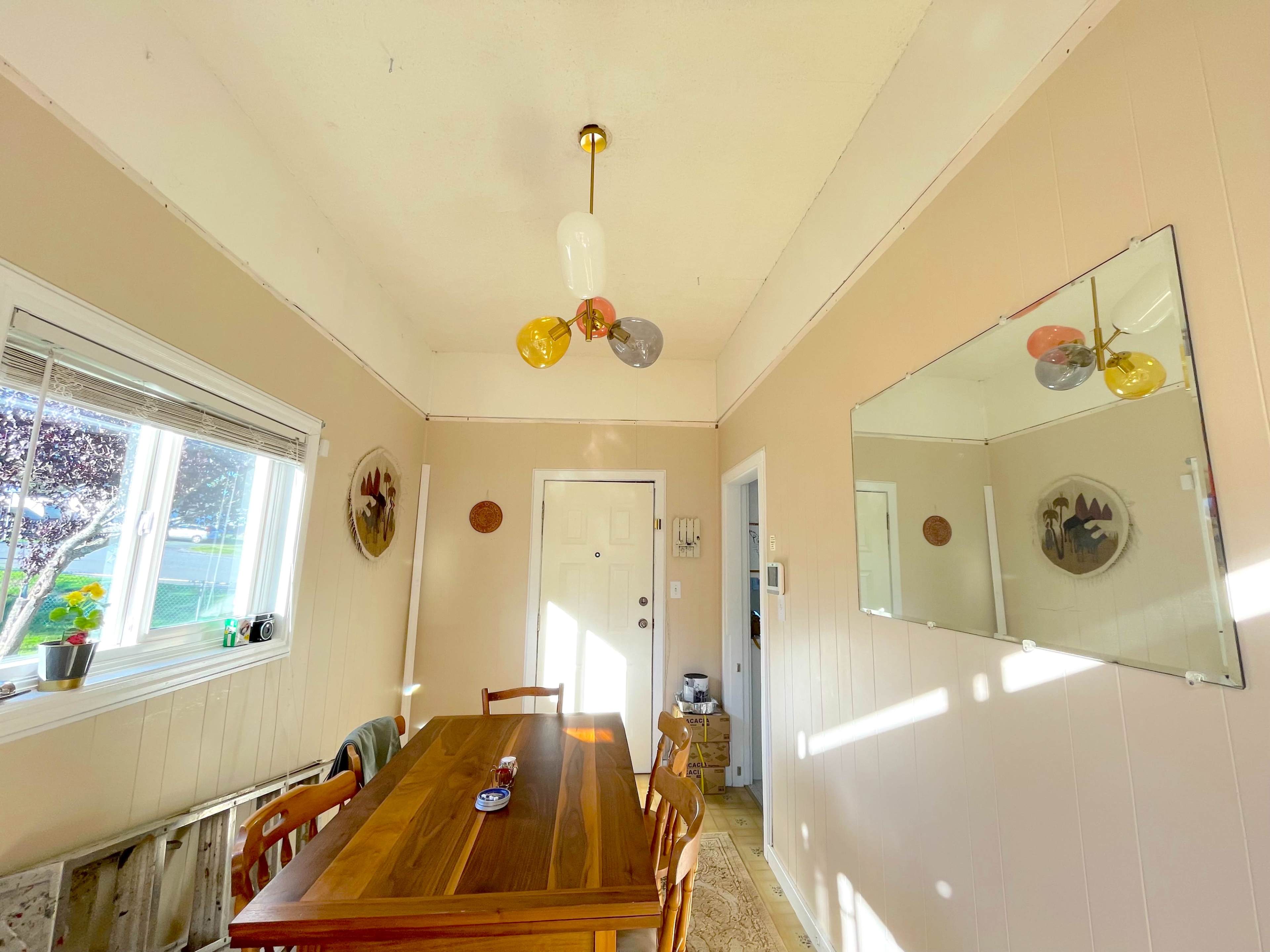A light-filled dining area with a wooden table, four chairs, and a ceiling light fixture with colorful bulbs.