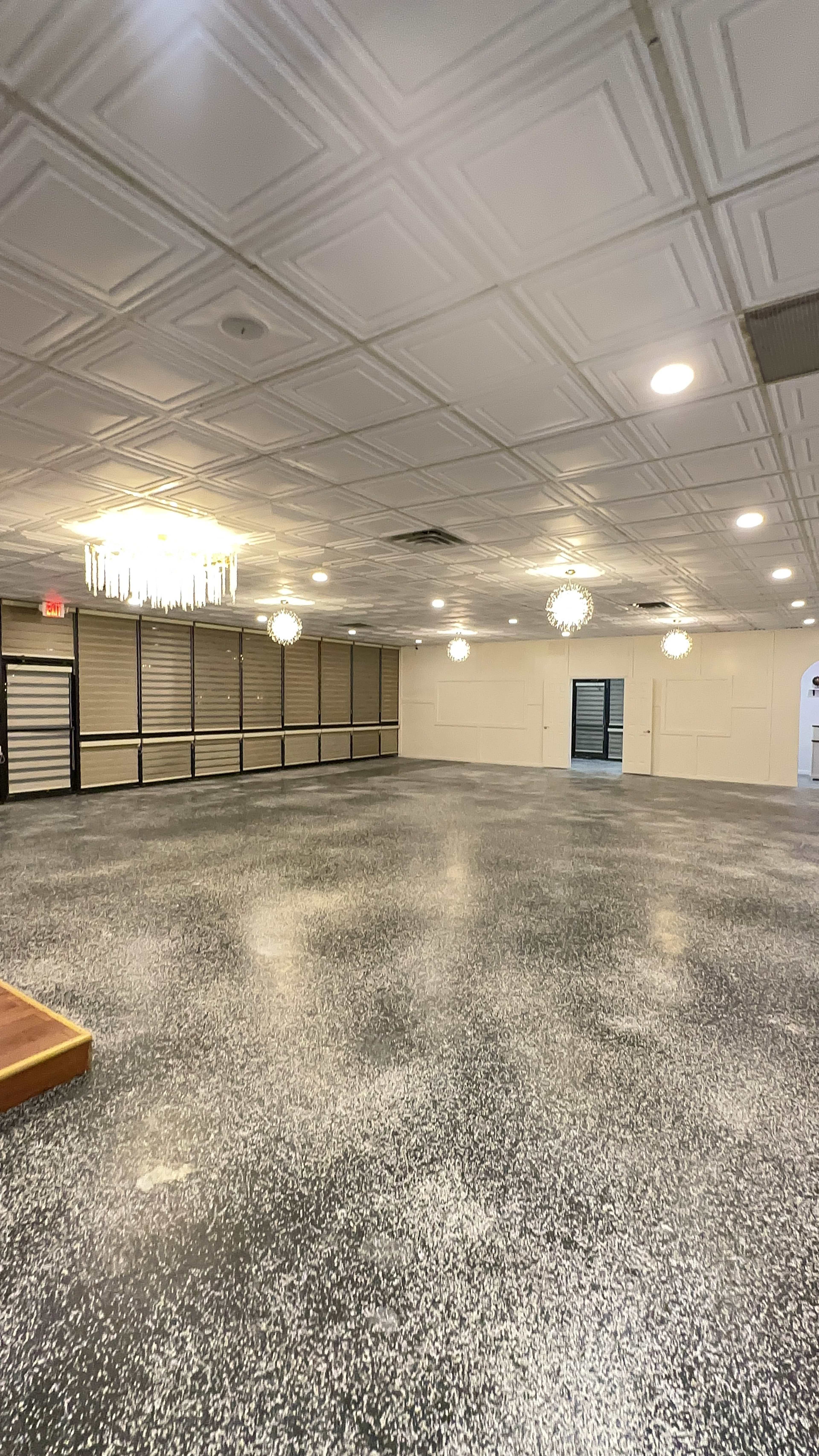 A spacious, empty room with a patterned ceiling, chandeliers, and a polished floor.
