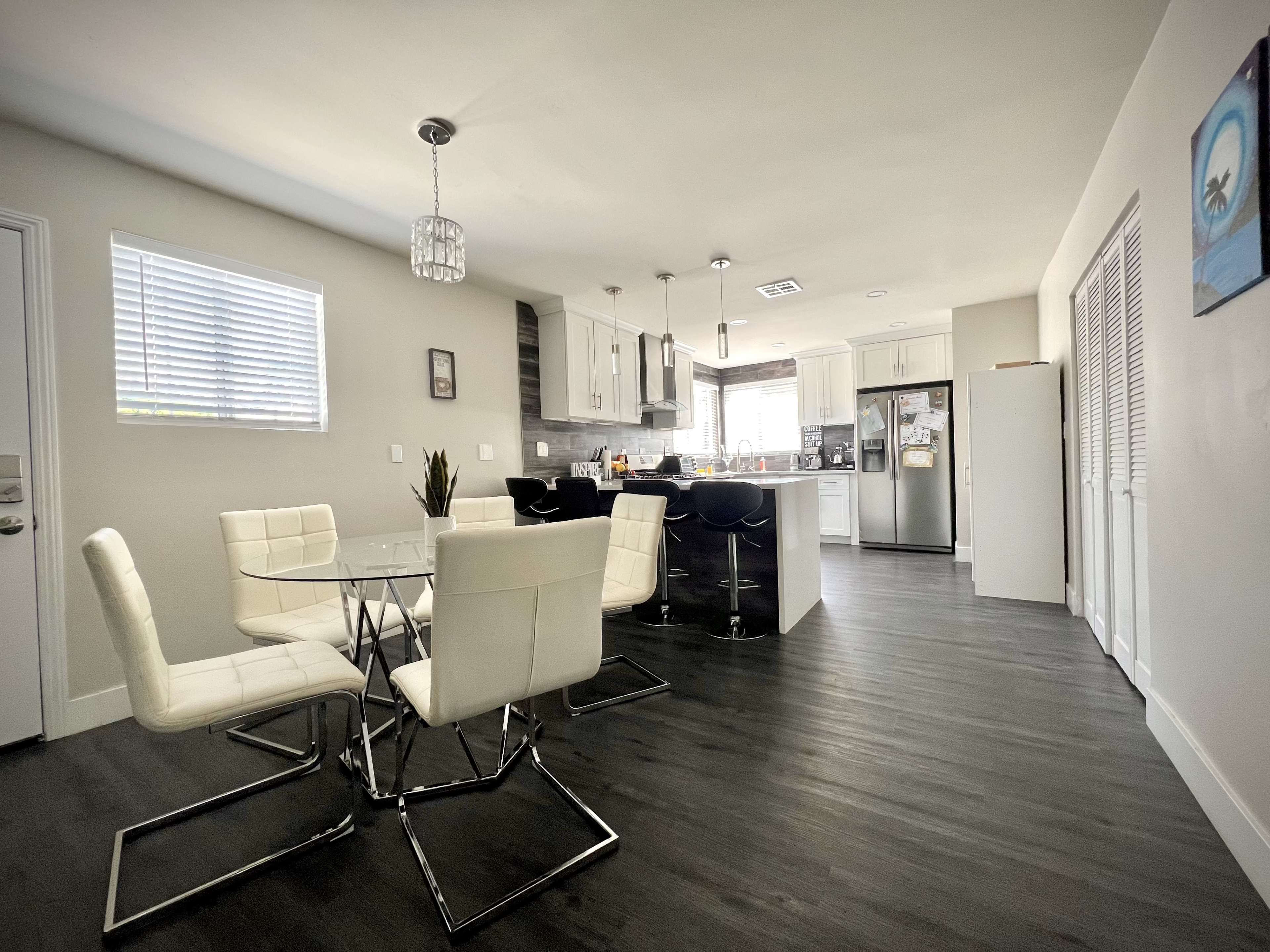 A modern kitchen and dining area feature a glass-top table with white chairs, a spacious island, and stainless steel appliances.