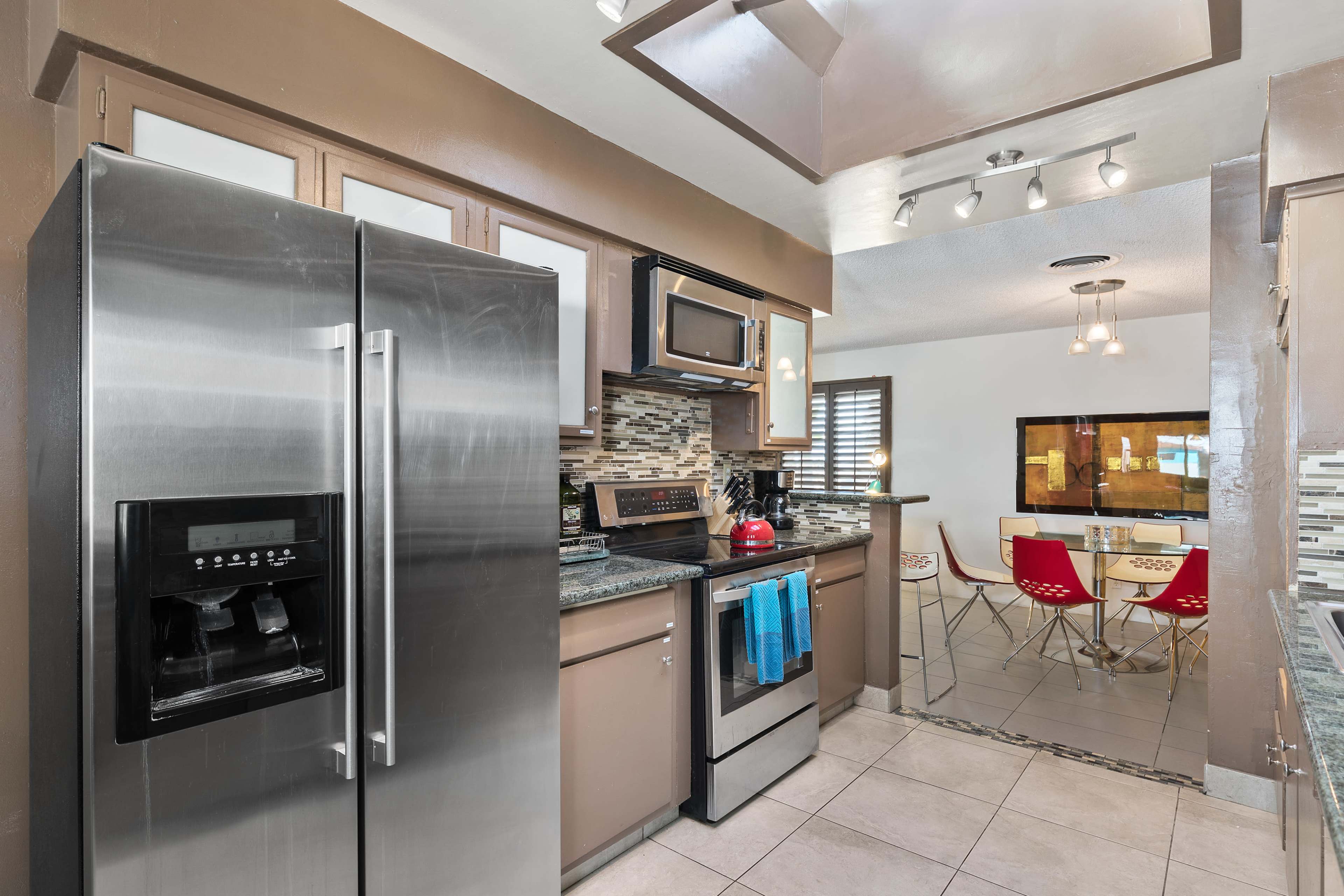 A modern kitchen with stainless steel appliances, granite countertops, and a dining area visible in the background.