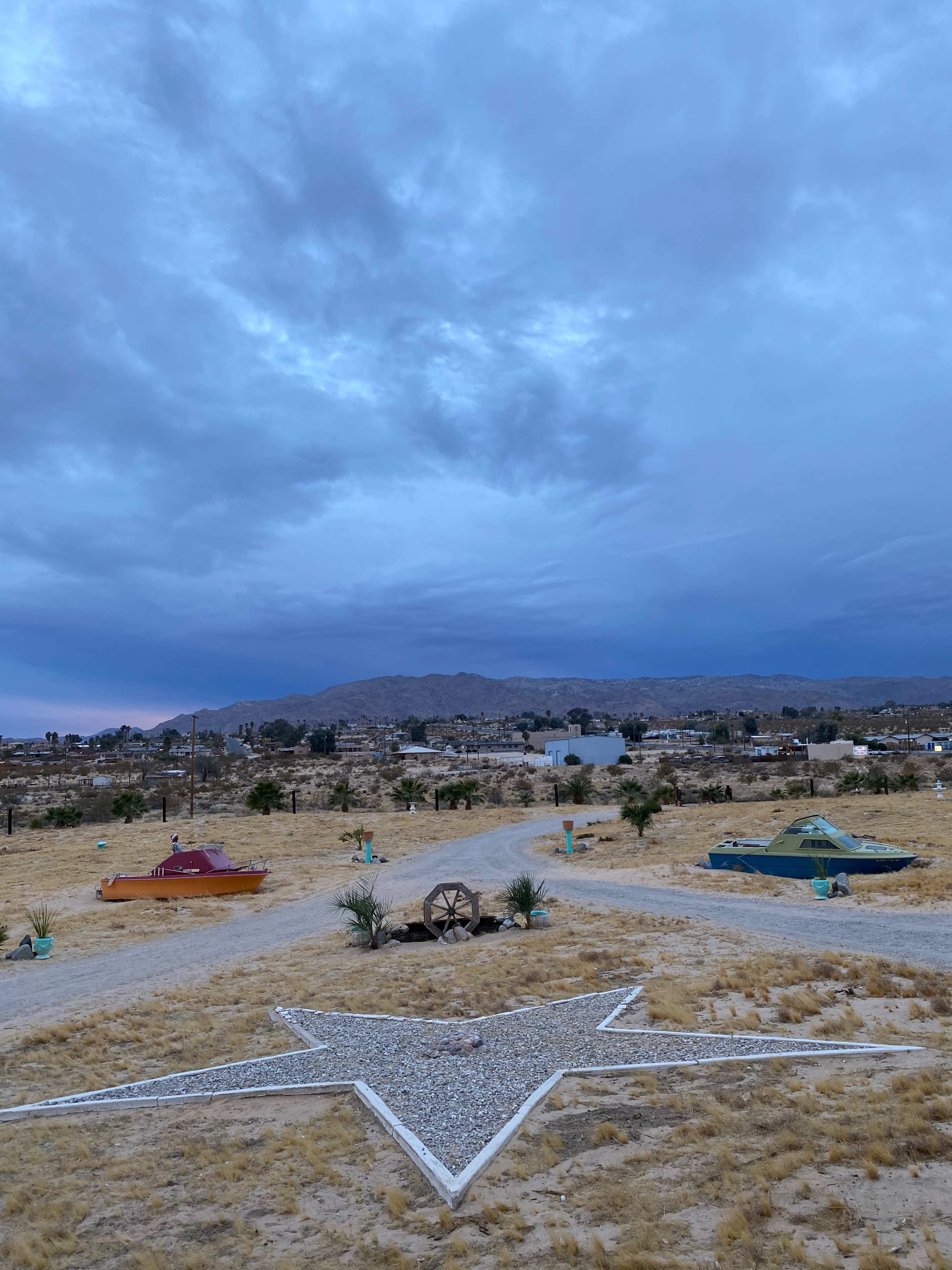 The scene captures a barren desert landscape featuring a prominent white star formation in the foreground, surrounded by colorful sculptures and mountains in the background under a cloudy sky.