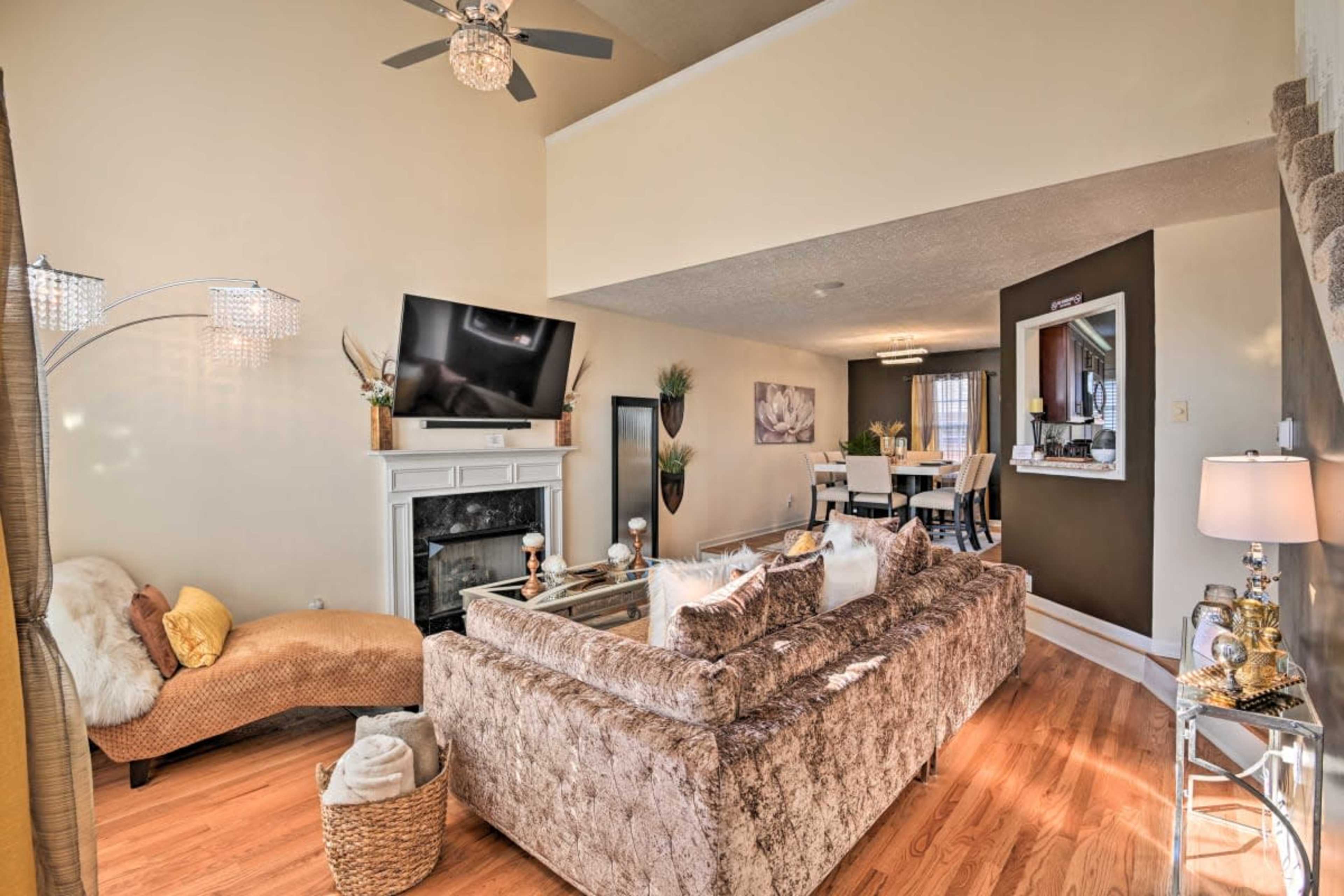 A modern living room with a large sectional sofa, a mounted television, and a staircase leading to an upper level, complemented by a dining area in the background.