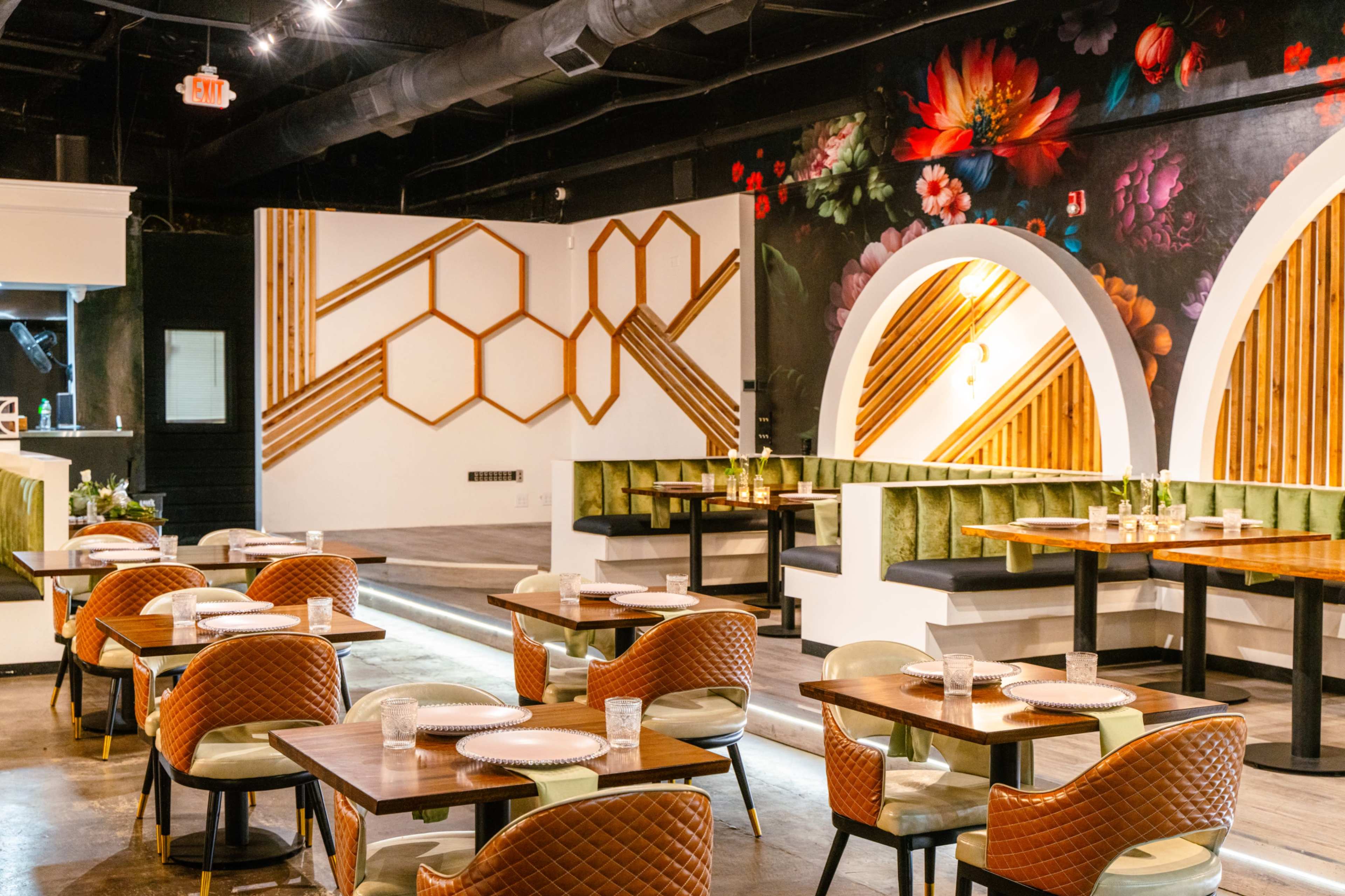 The image shows a modern restaurant interior featuring wooden hexagonal designs on the walls, green upholstered seating, and tables set with plates and glasses.