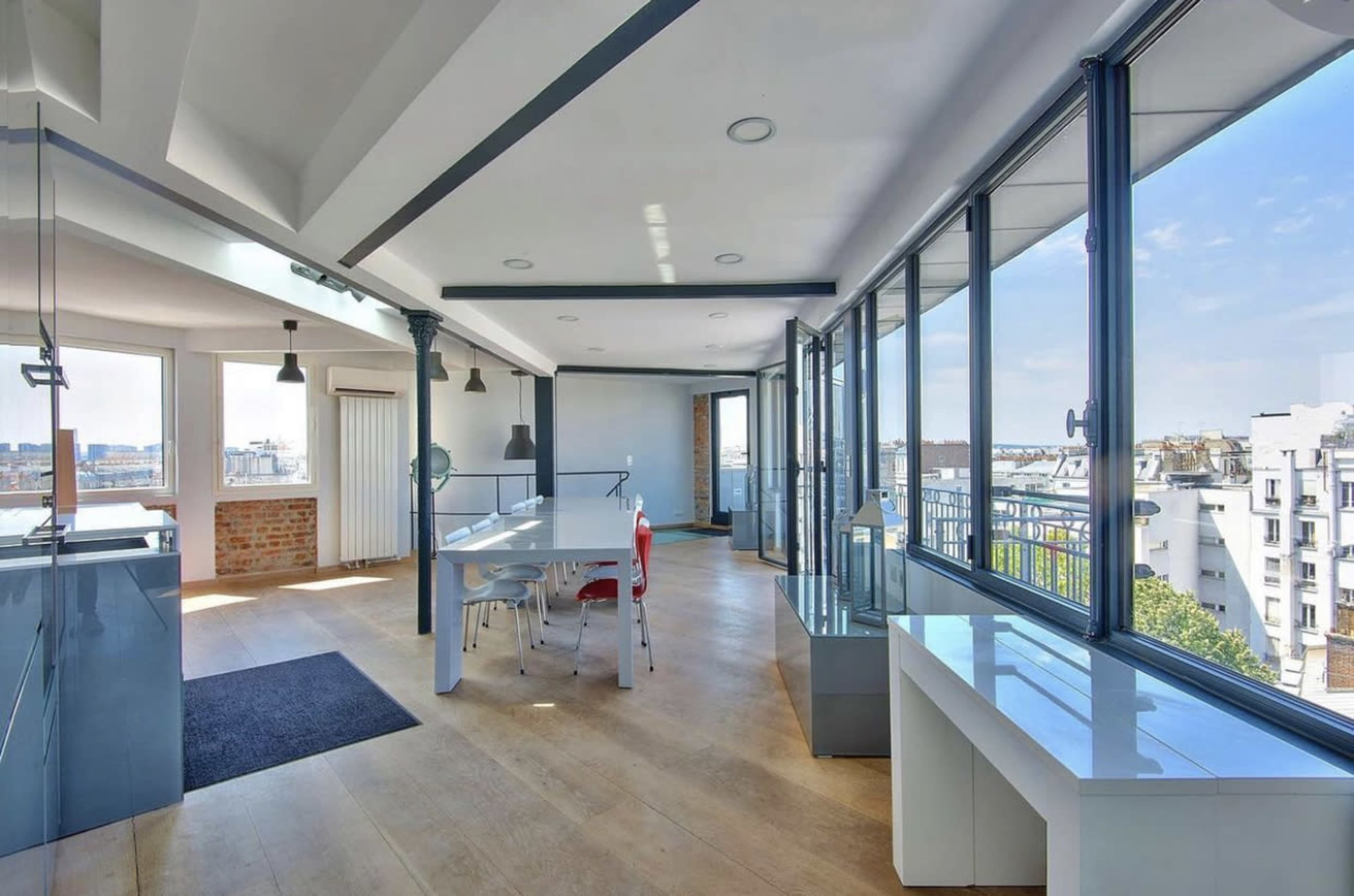 The image shows a modern, open-concept living space with large windows that provide natural light and a view of the city.