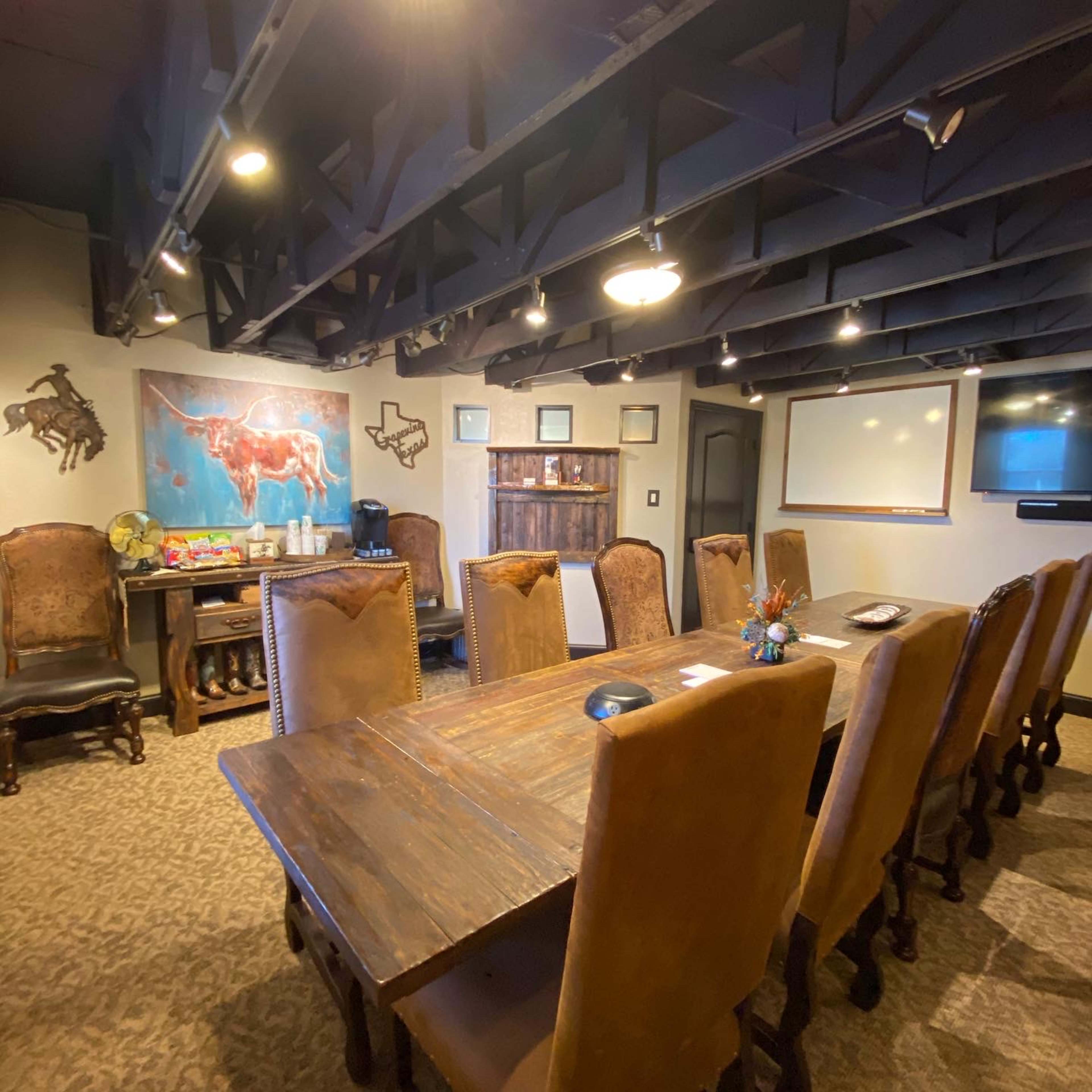A conference room with a large wooden table surrounded by high-backed chairs, featuring a Texas-themed mural and visible technology such as a whiteboard and monitor.