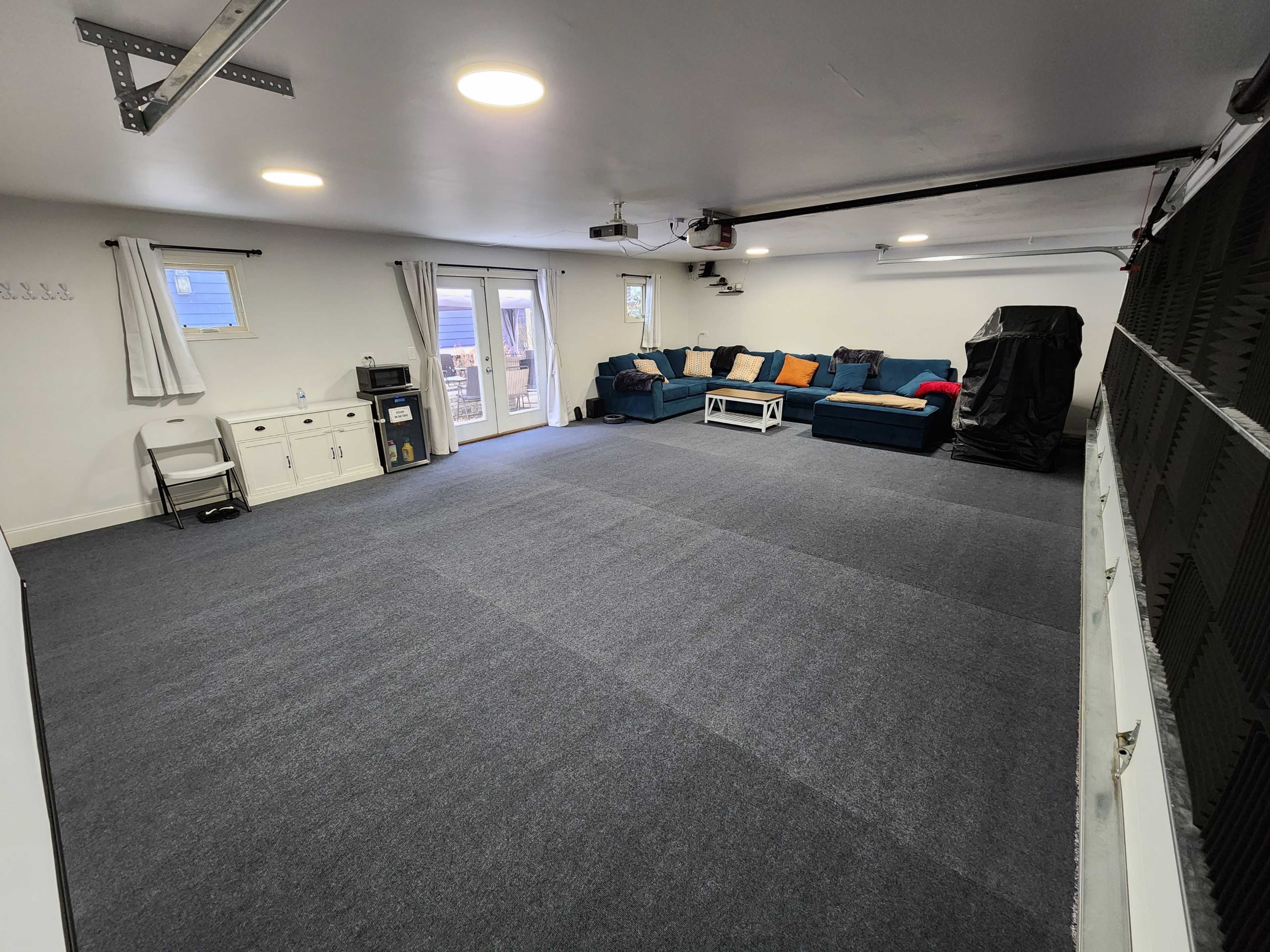 A large, empty room with gray carpet, a blue sectional sofa, a coffee table, and a sliding door leading to an outdoor area.