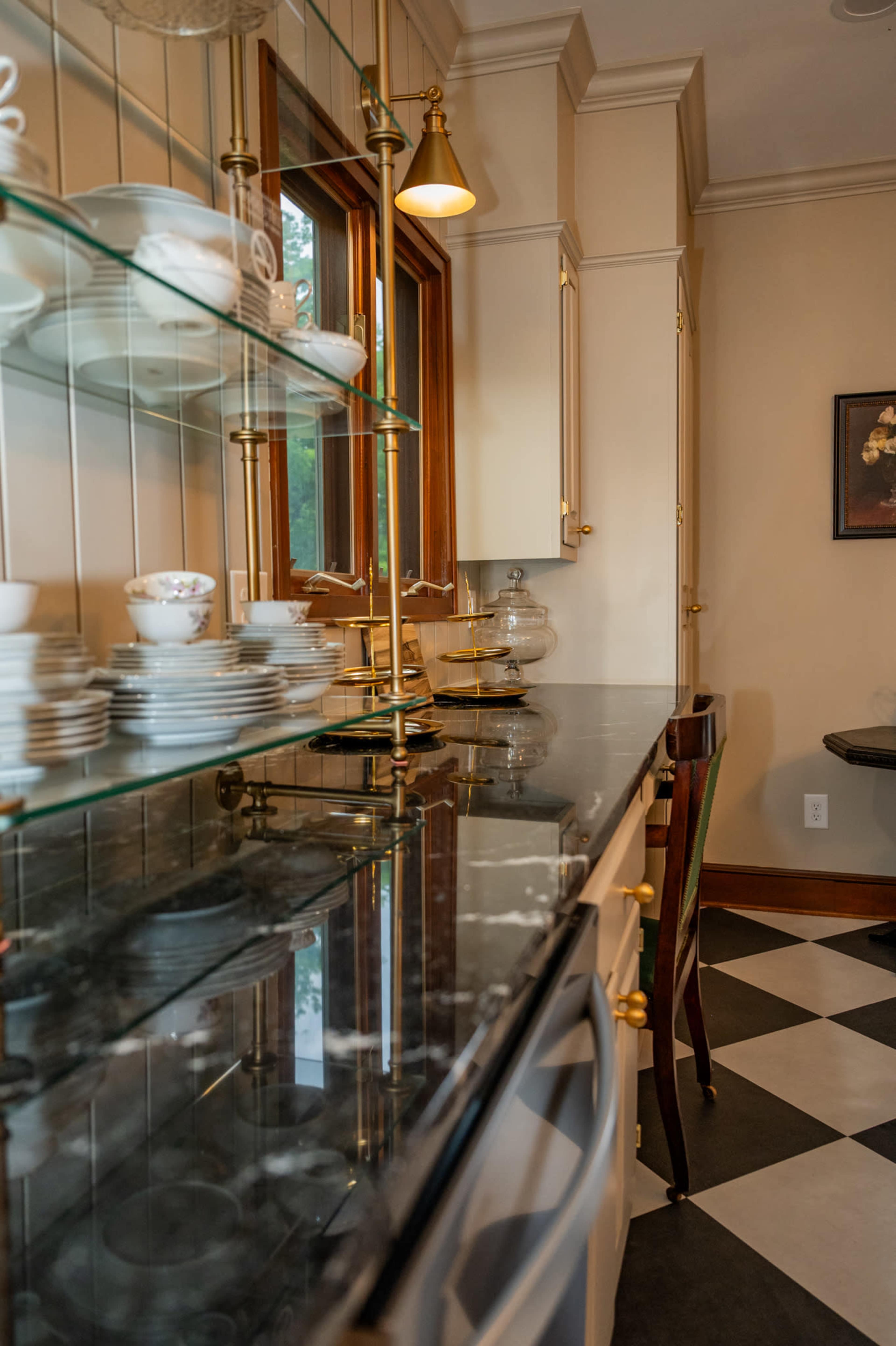 The image shows a kitchen with a marble countertop, glass shelves displaying dishware, and black and white checkered flooring.
