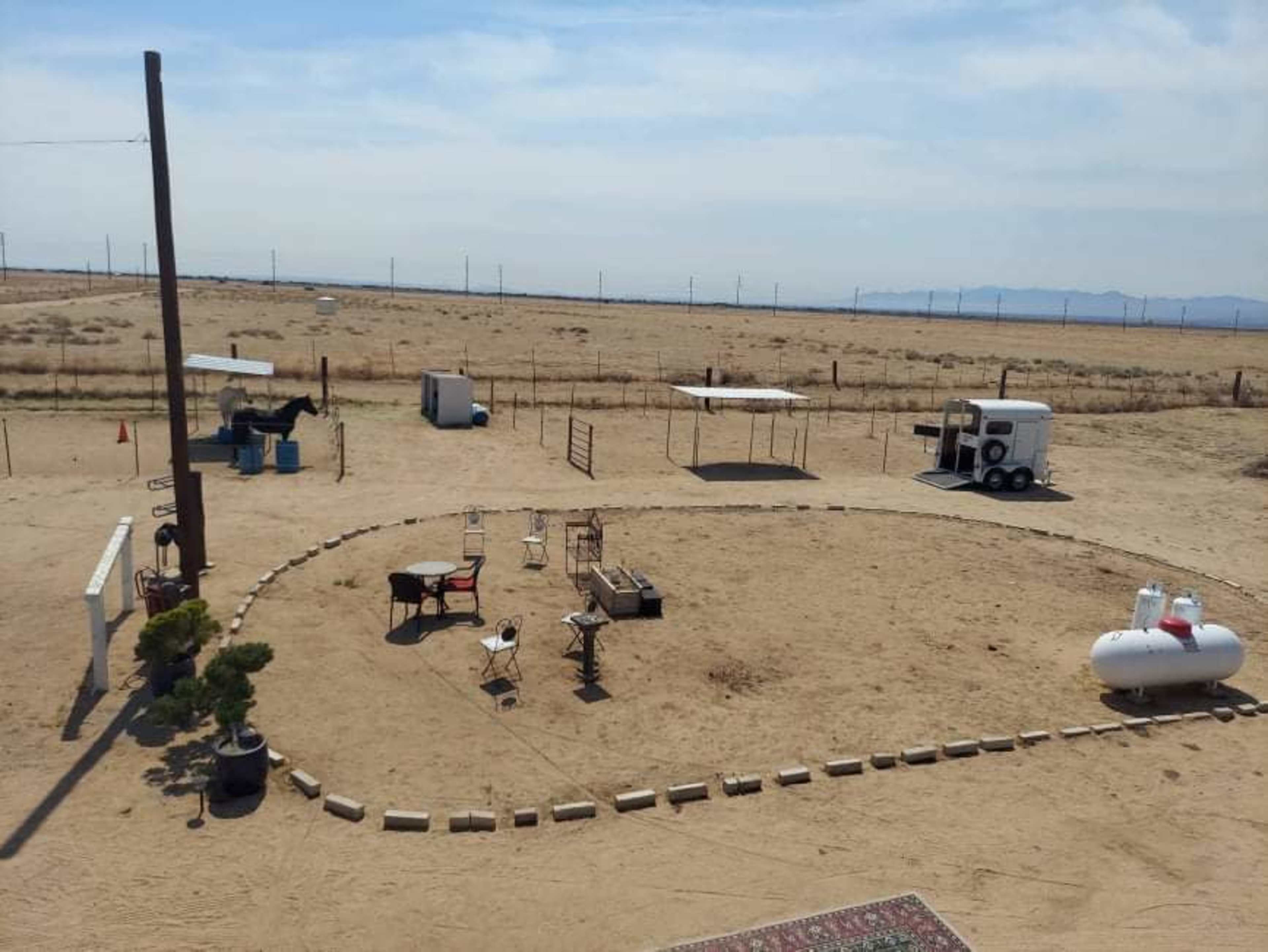 A barren, sandy area with sparse furniture and structures arranged in a circular layout.