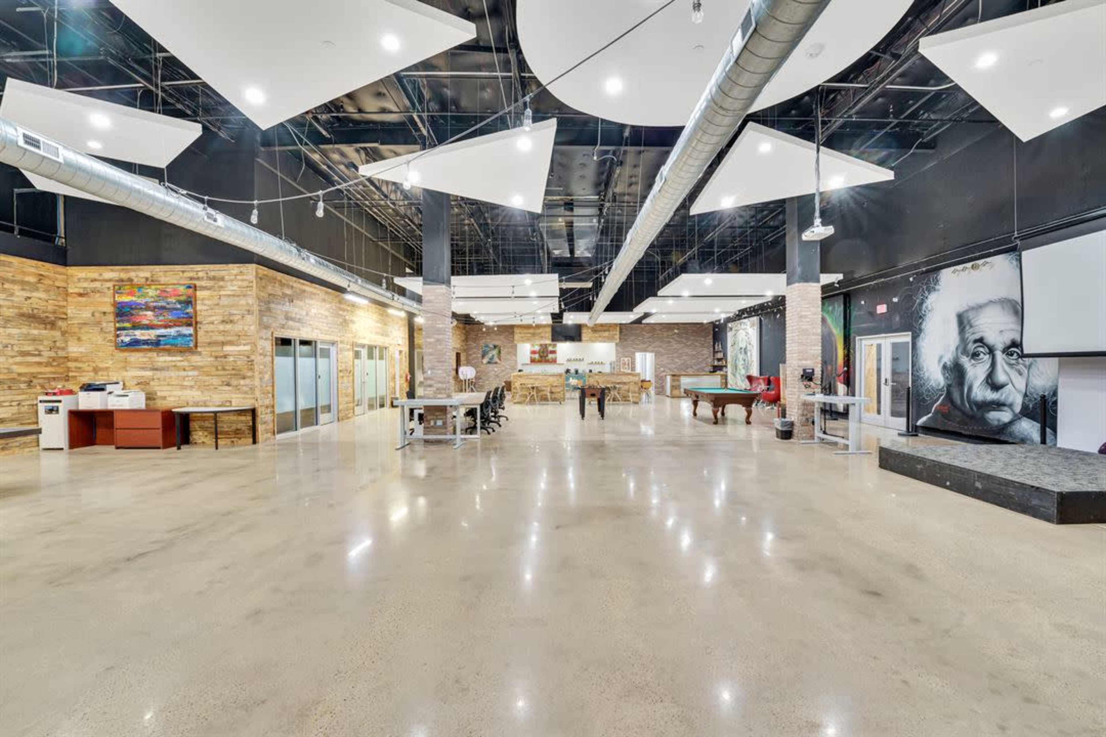 A spacious interior with polished concrete floors, wooden accent walls, and large artwork, featuring pool tables and seating areas.