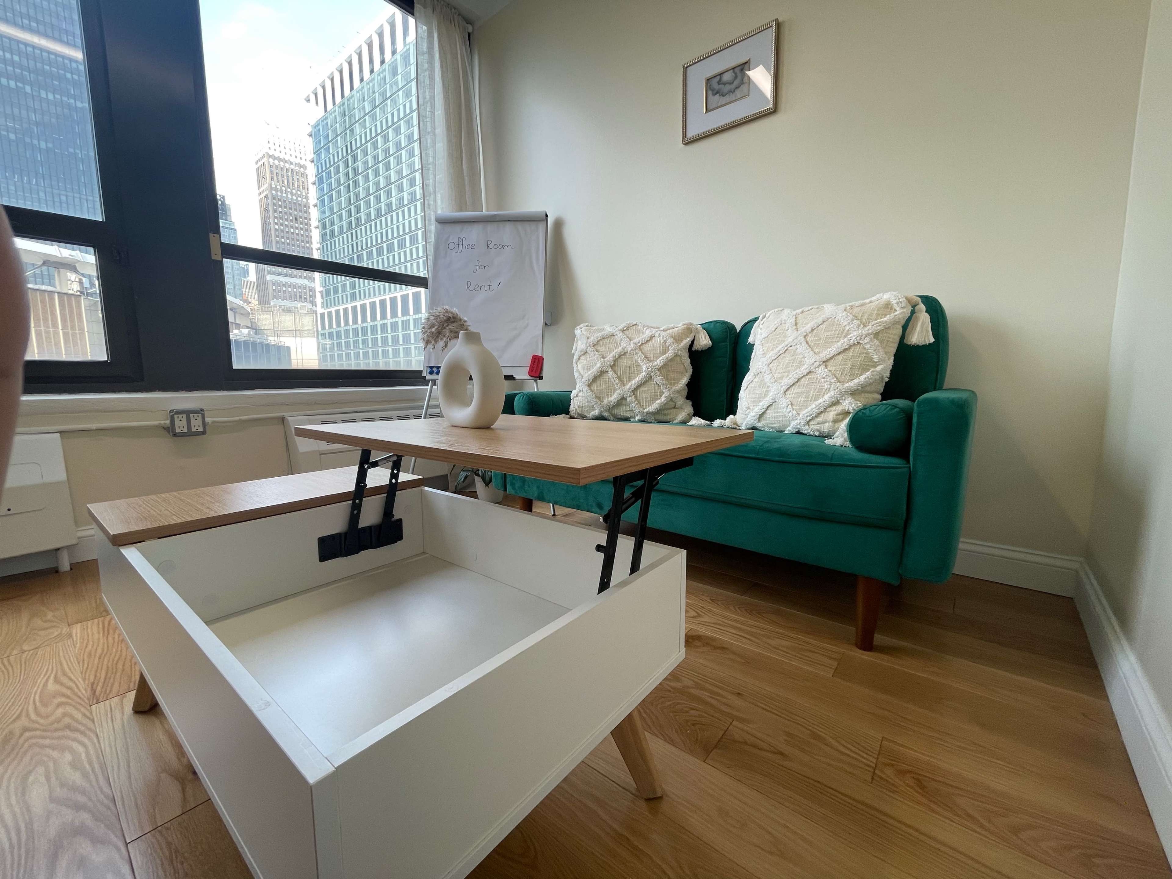 A modern living room with a green couch and a coffee table that has a lift-top, positioned next to a whiteboard.