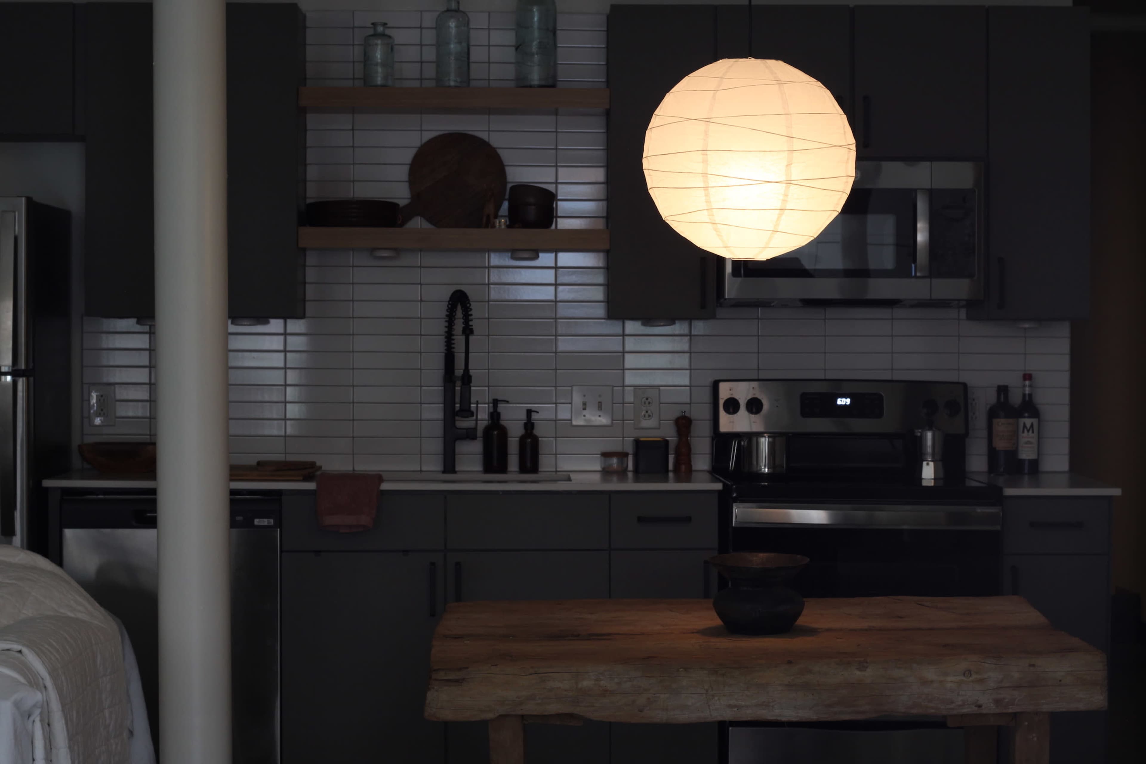 A pendant light hangs above a wooden table in a modern kitchen with gray cabinetry and stainless steel appliances.