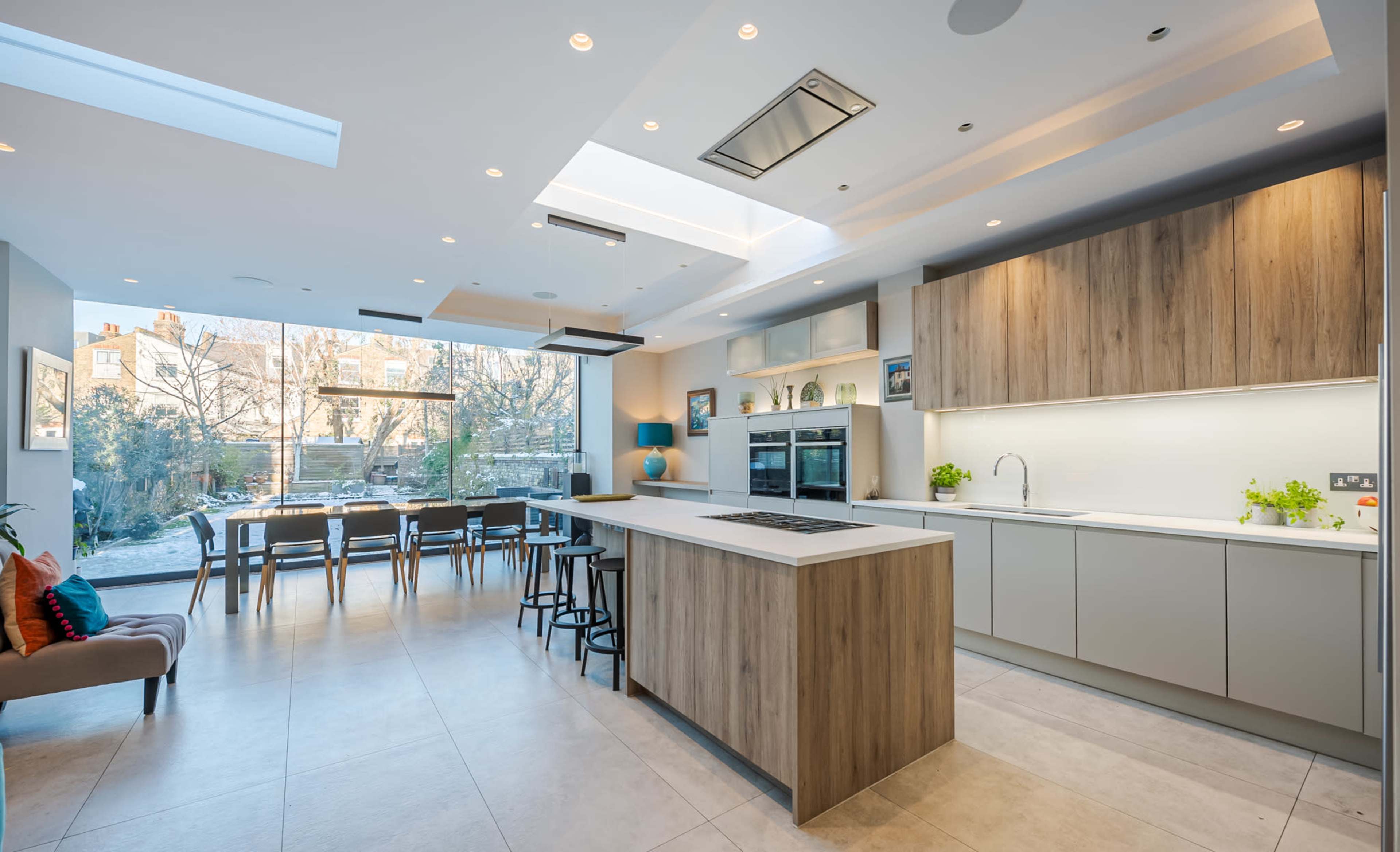 A modern kitchen with an island, sleek cabinetry, and a large window overlooking an outdoor dining area.