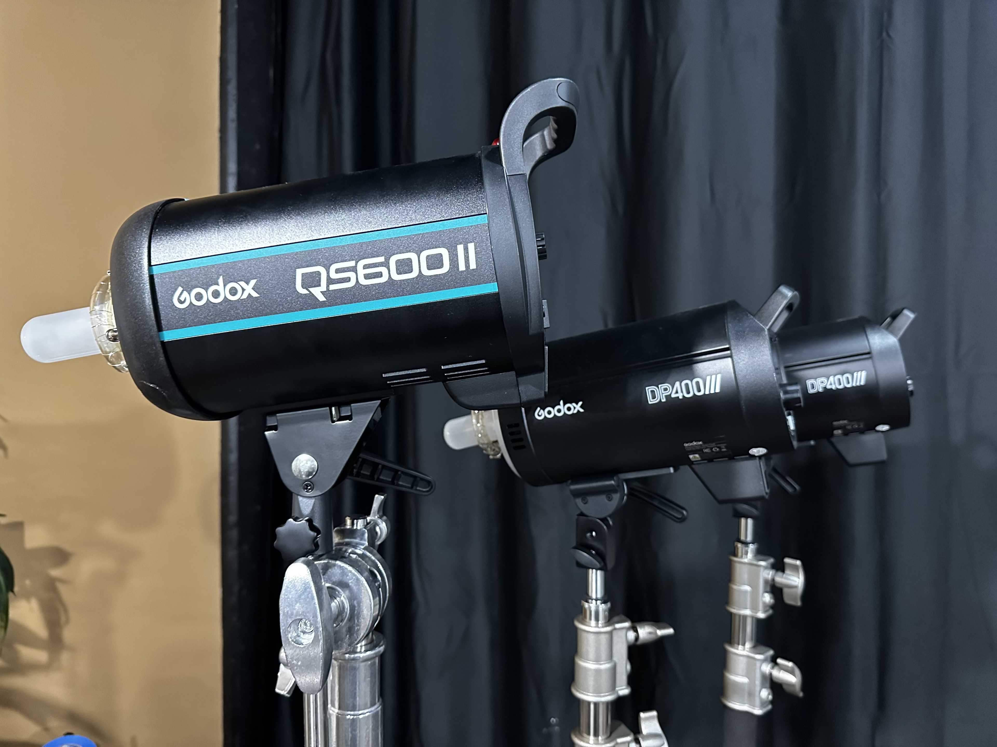 Two Godox studio flash lighting units mounted on stands against a dark backdrop.
