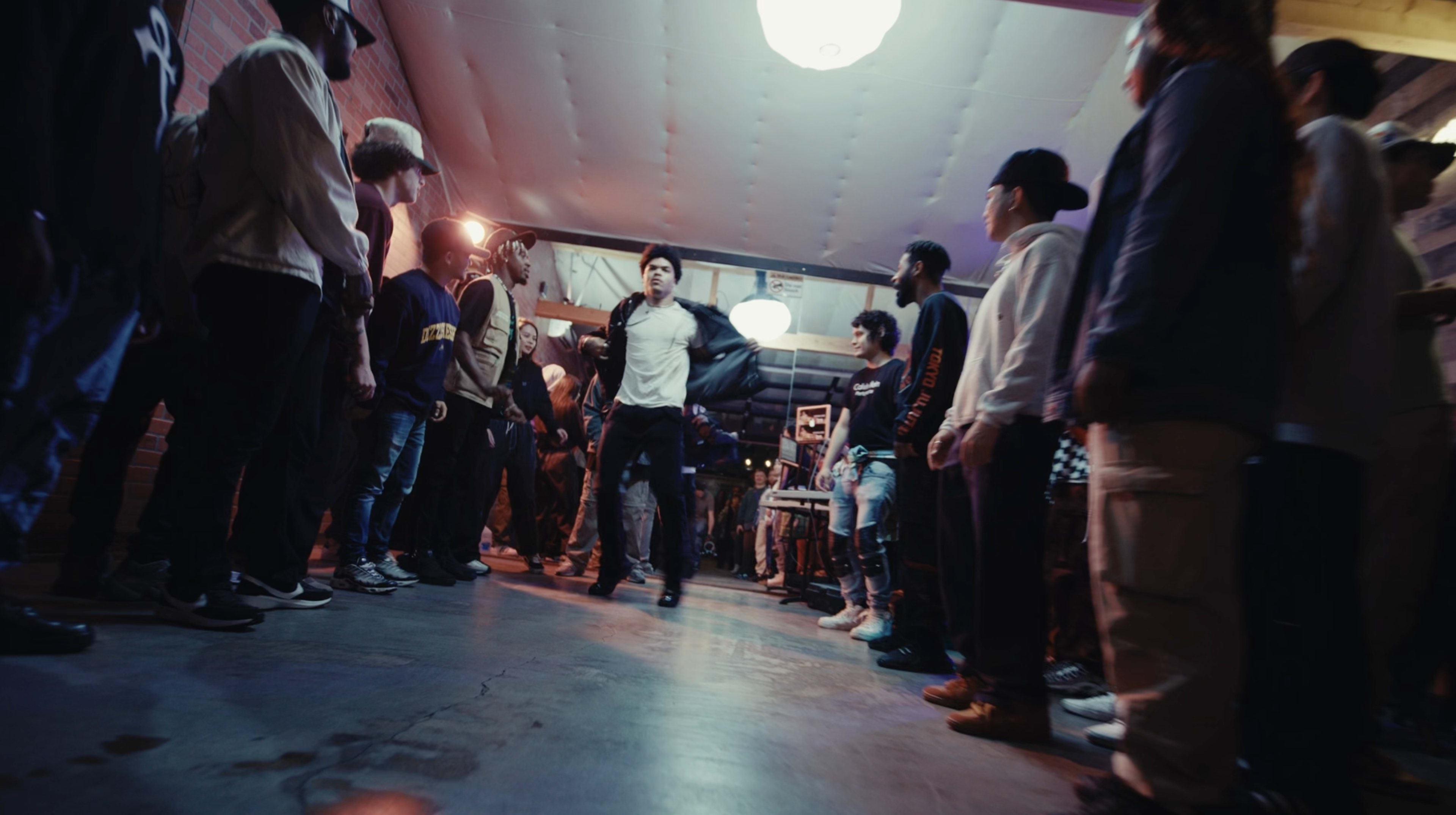 A group of people surrounds a dancer performing in a dimly lit venue while others watch attentively.