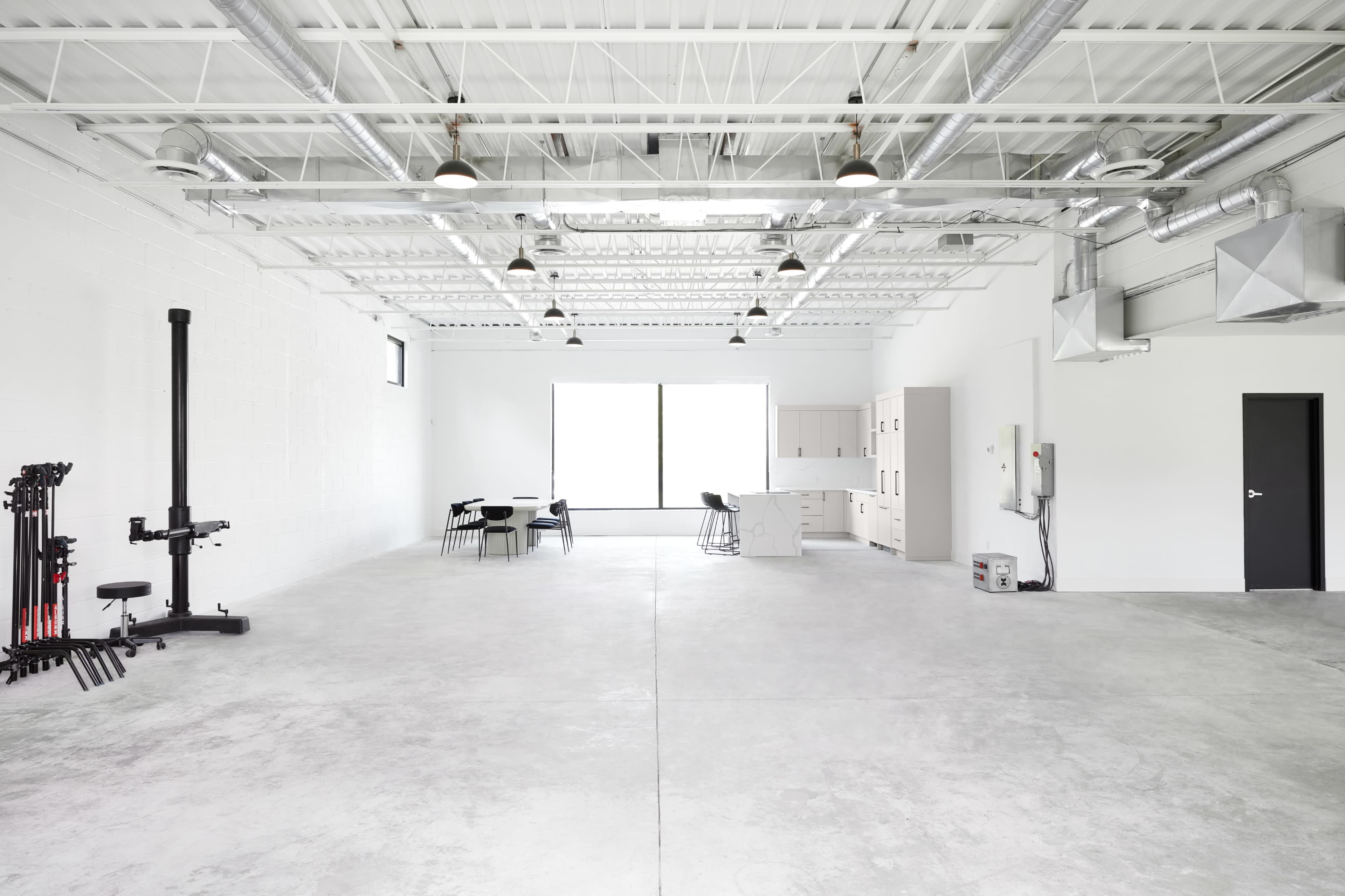 A spacious, empty room with concrete flooring and large windows, featuring a workout station on the left and modular furniture on the right.