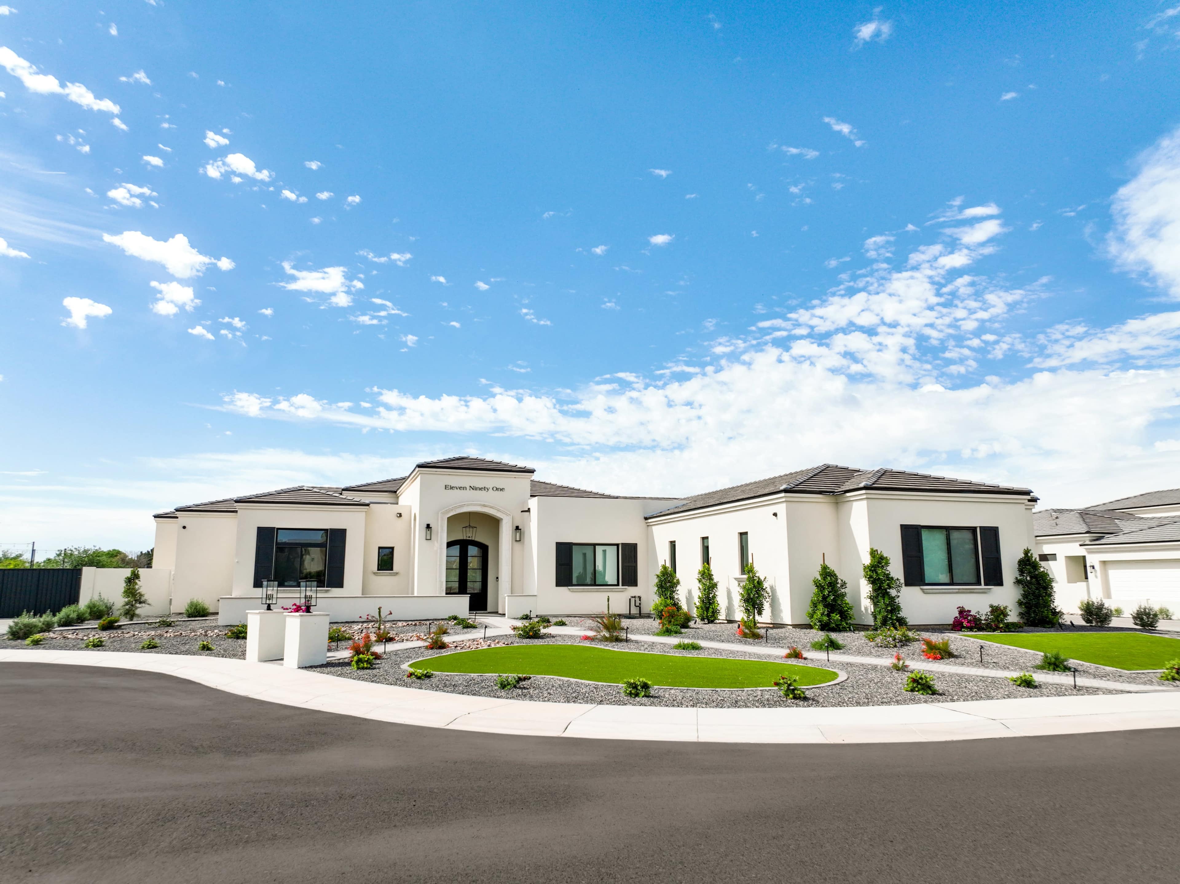 A modern single-story house features a spacious front yard with landscaped gardens and a circular driveway under a clear blue sky.