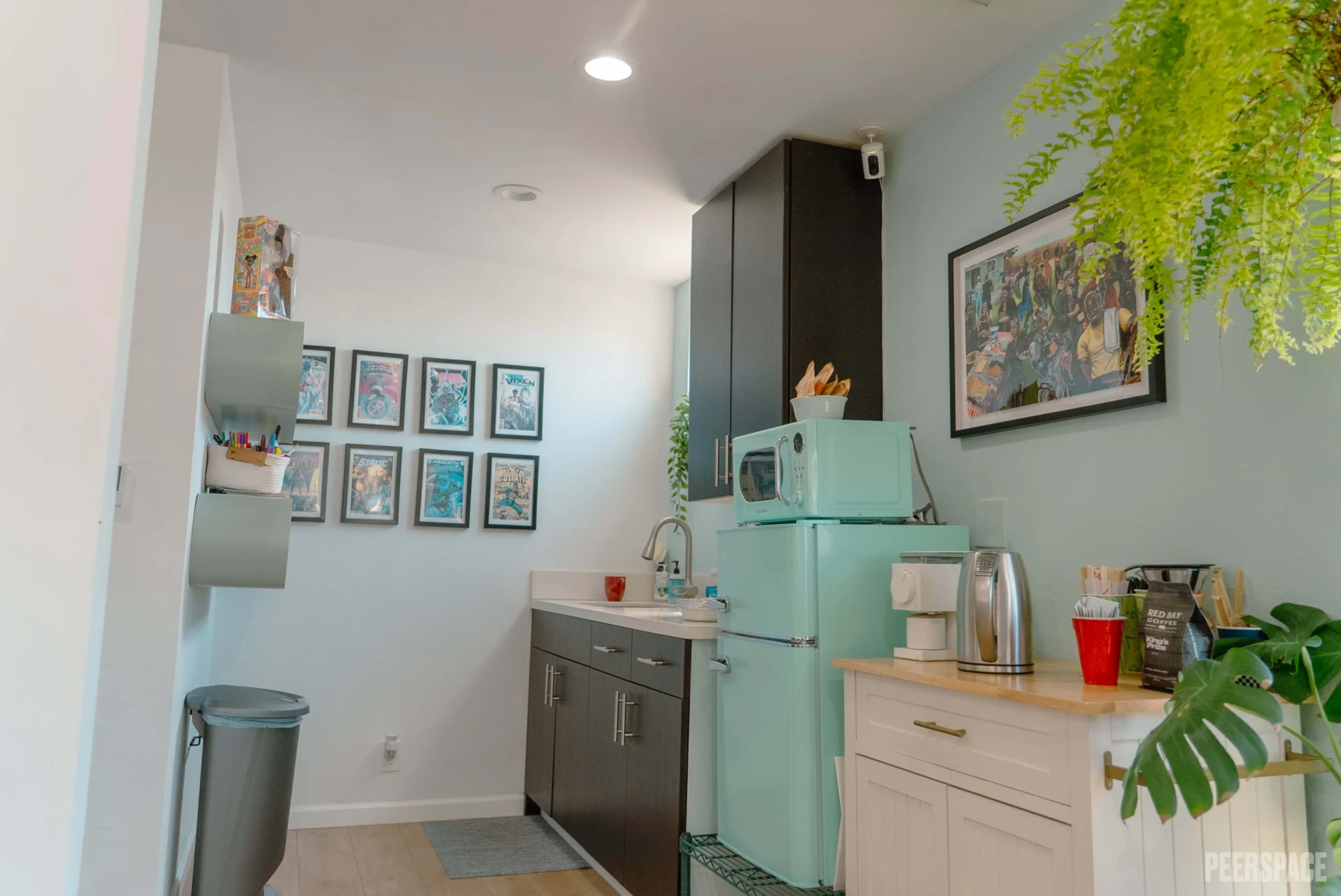 The image shows a modern kitchen space featuring a light blue refrigerator, a sink with utensils, and framed artwork on the wall.