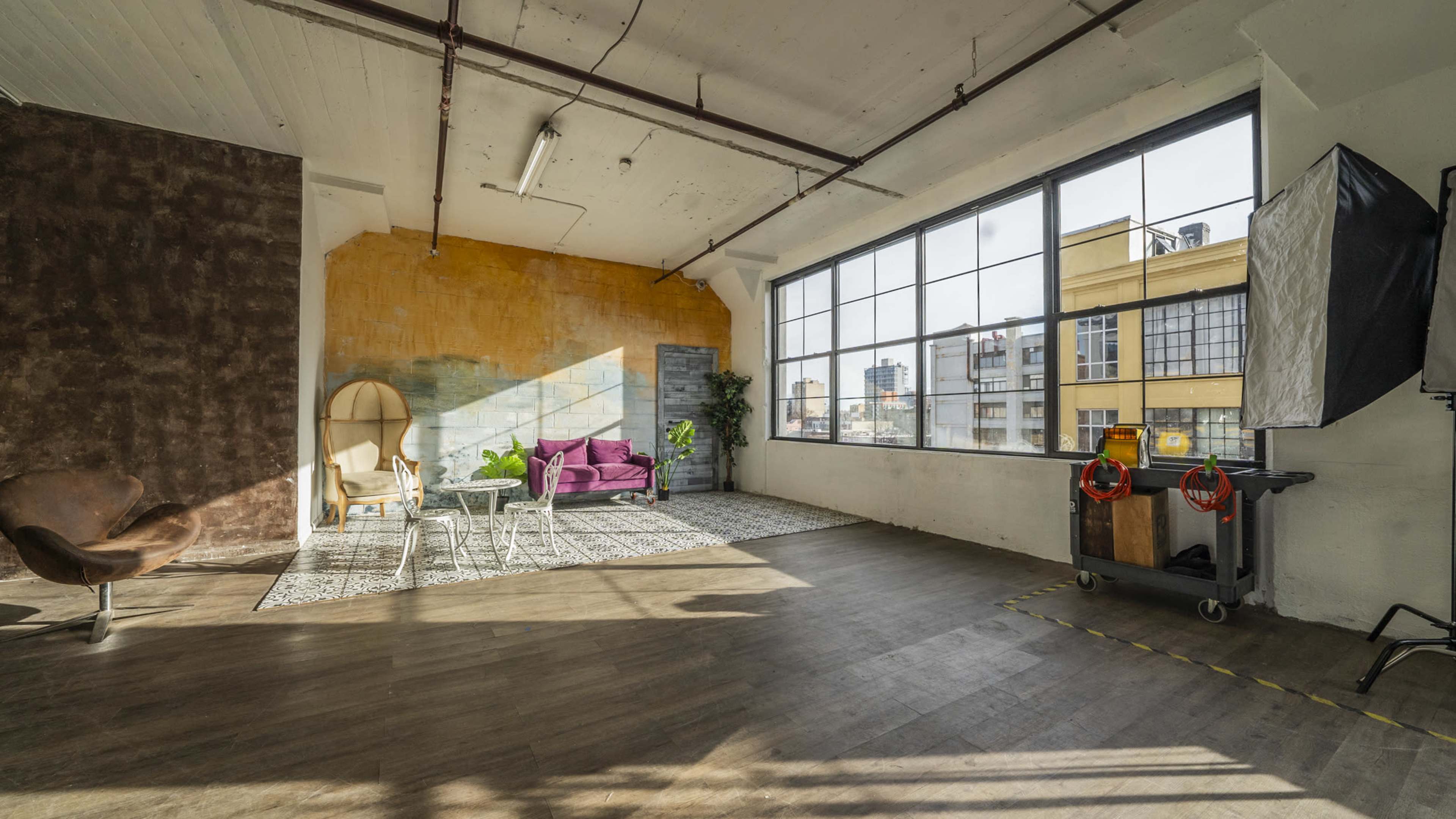 A spacious interior features large windows, a seating area with a purple couch, a wooden floor, and a variety of decorative elements.