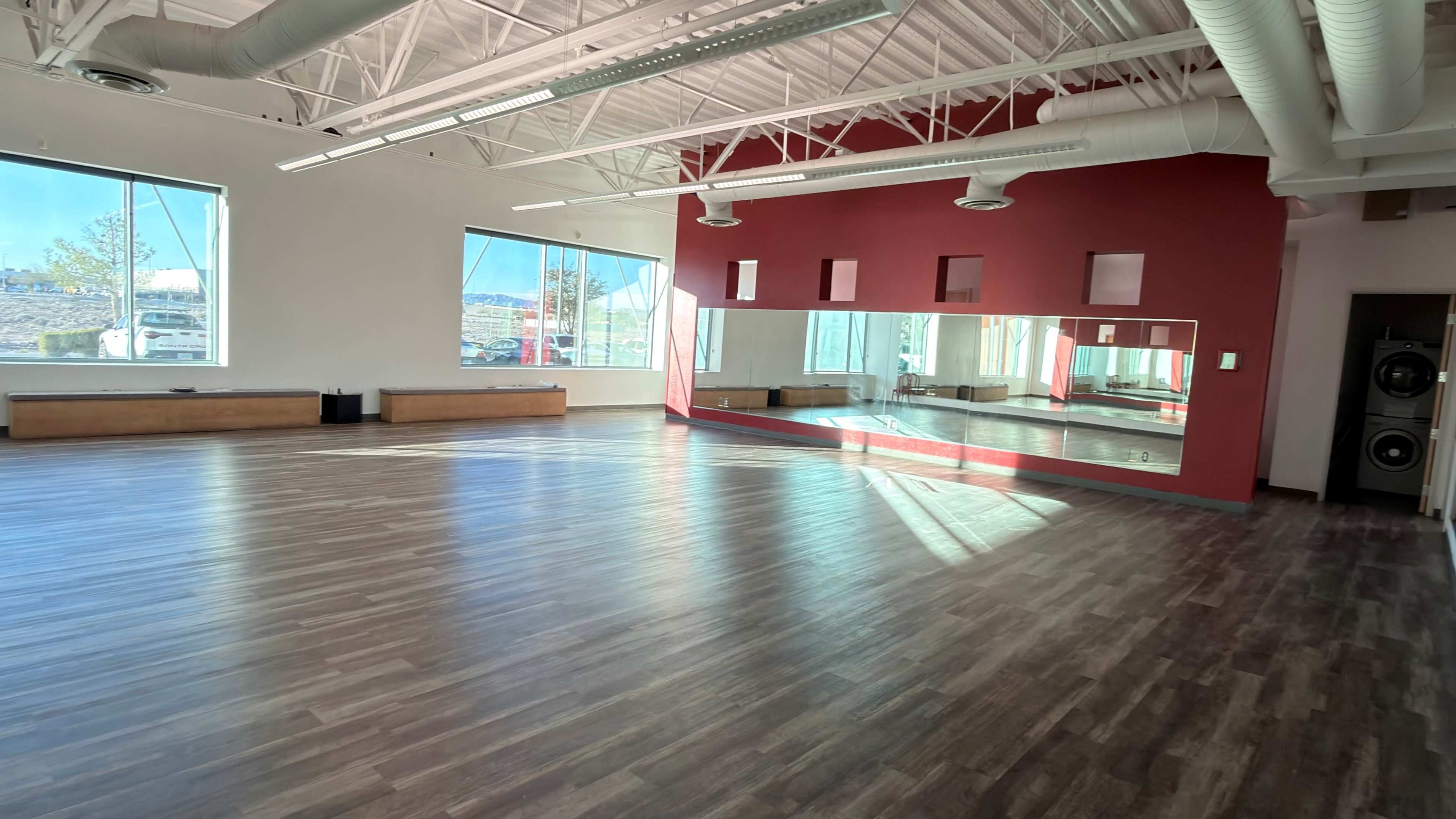 The image shows a spacious dance studio with large windows, hardwood flooring, and a mirrored wall on one side.