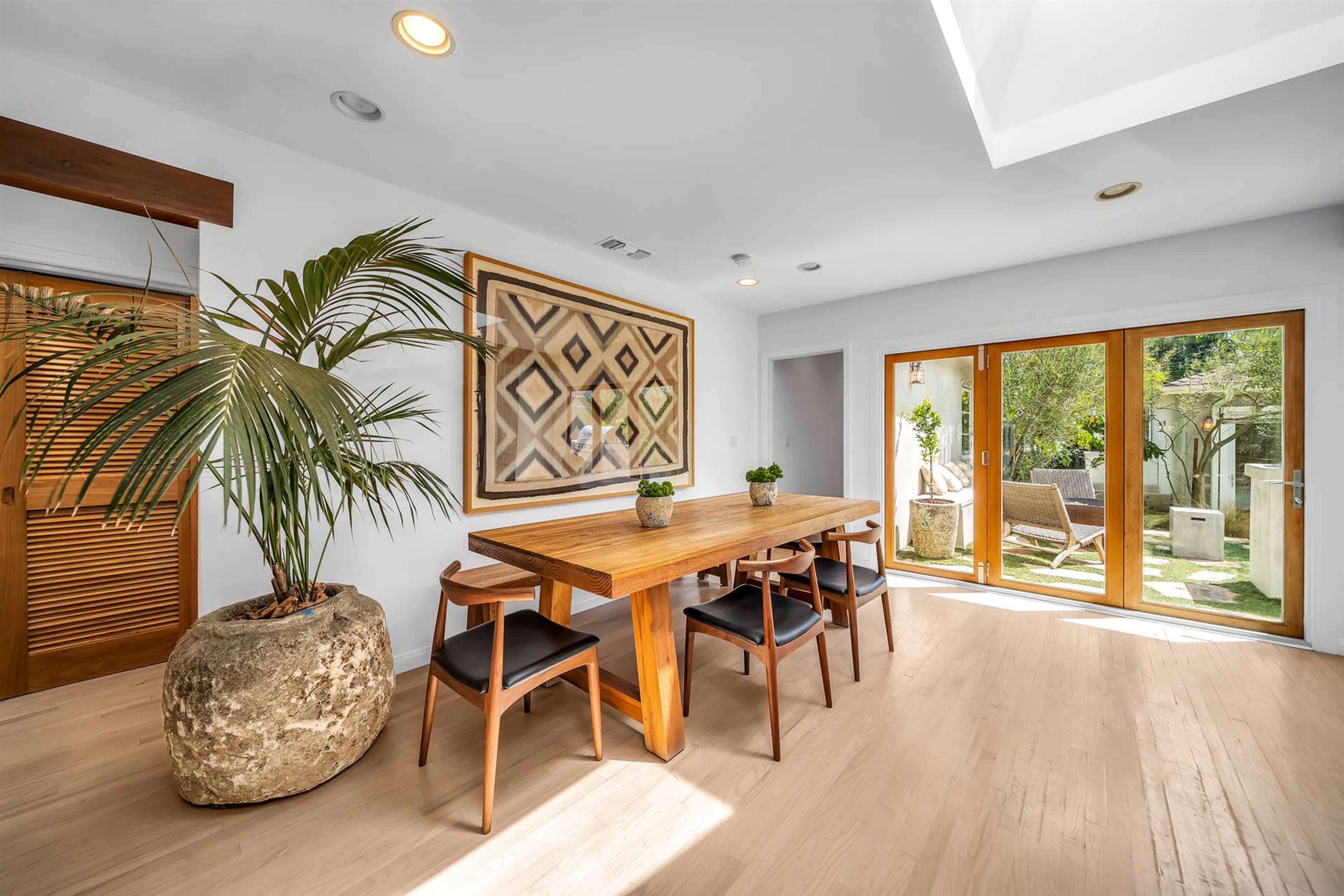 A dining area features a wooden table surrounded by black chairs, with sliding glass doors opening to a garden.
