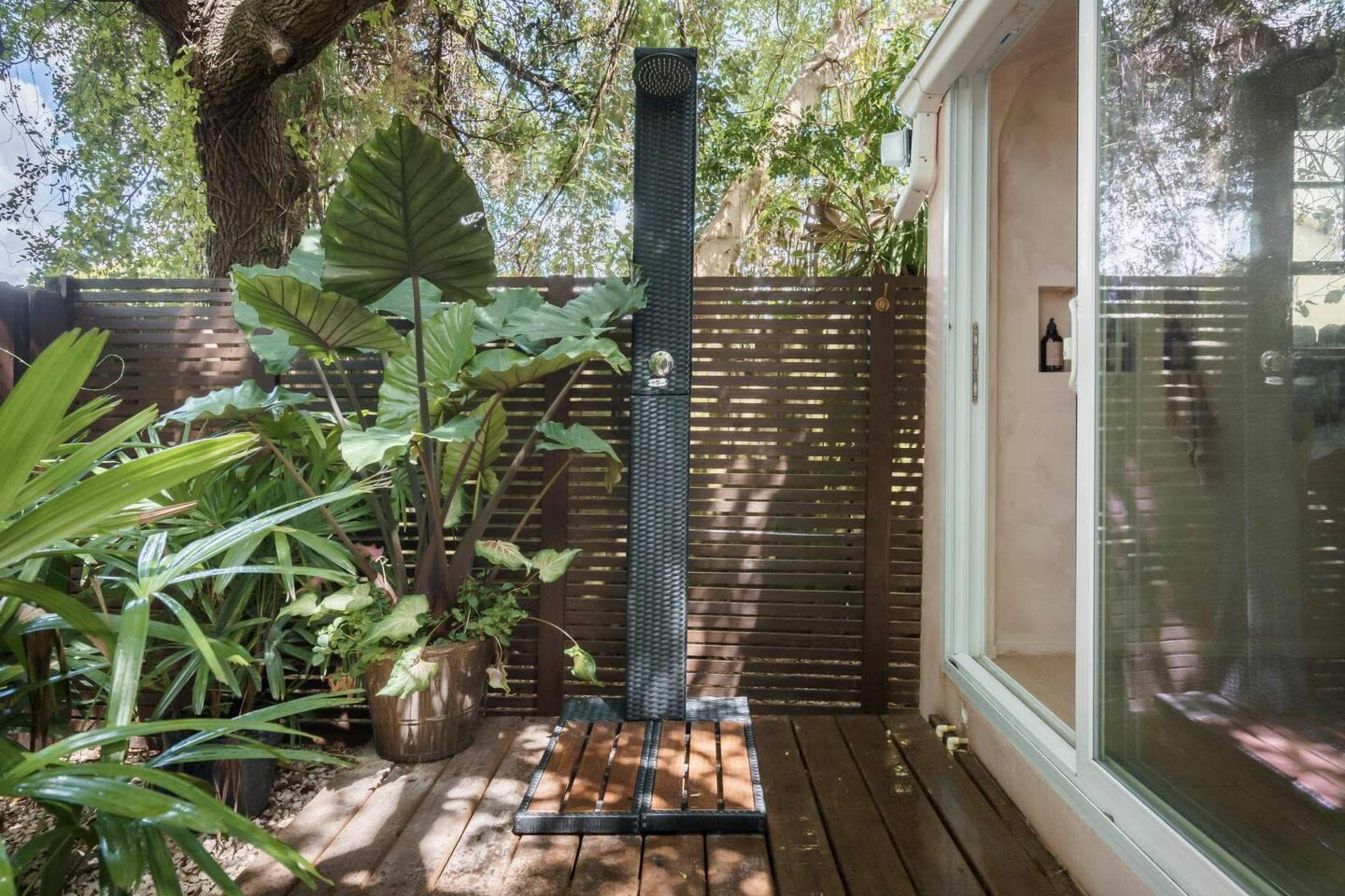 An outdoor shower surrounded by lush greenery and wooden slats for privacy.