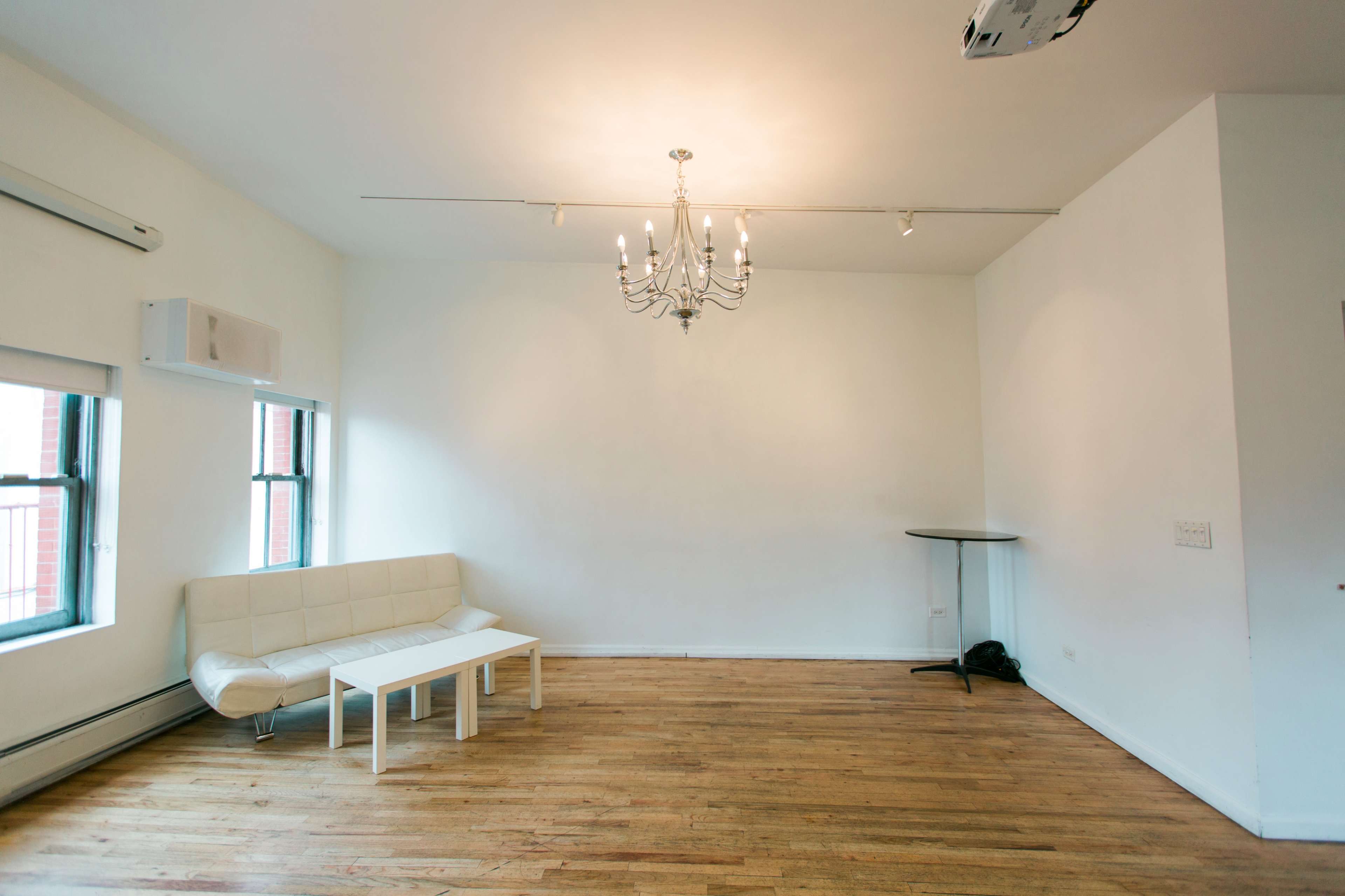 The image shows a sparsely furnished room with a white couch, a small table, and a chandelier hanging from the ceiling.