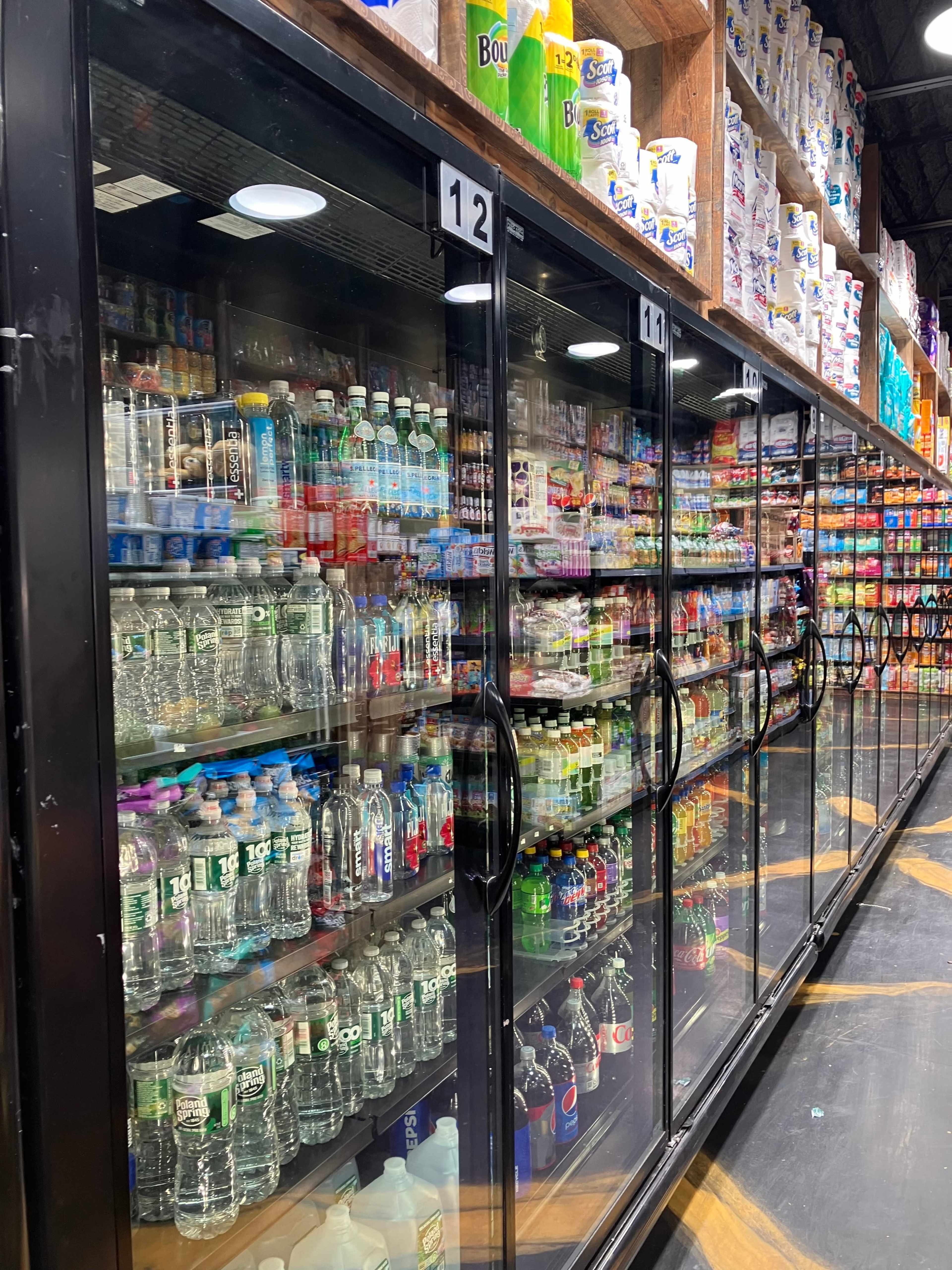 A row of glass-fronted display refrigerators filled with various bottled beverages and snack items in a store.