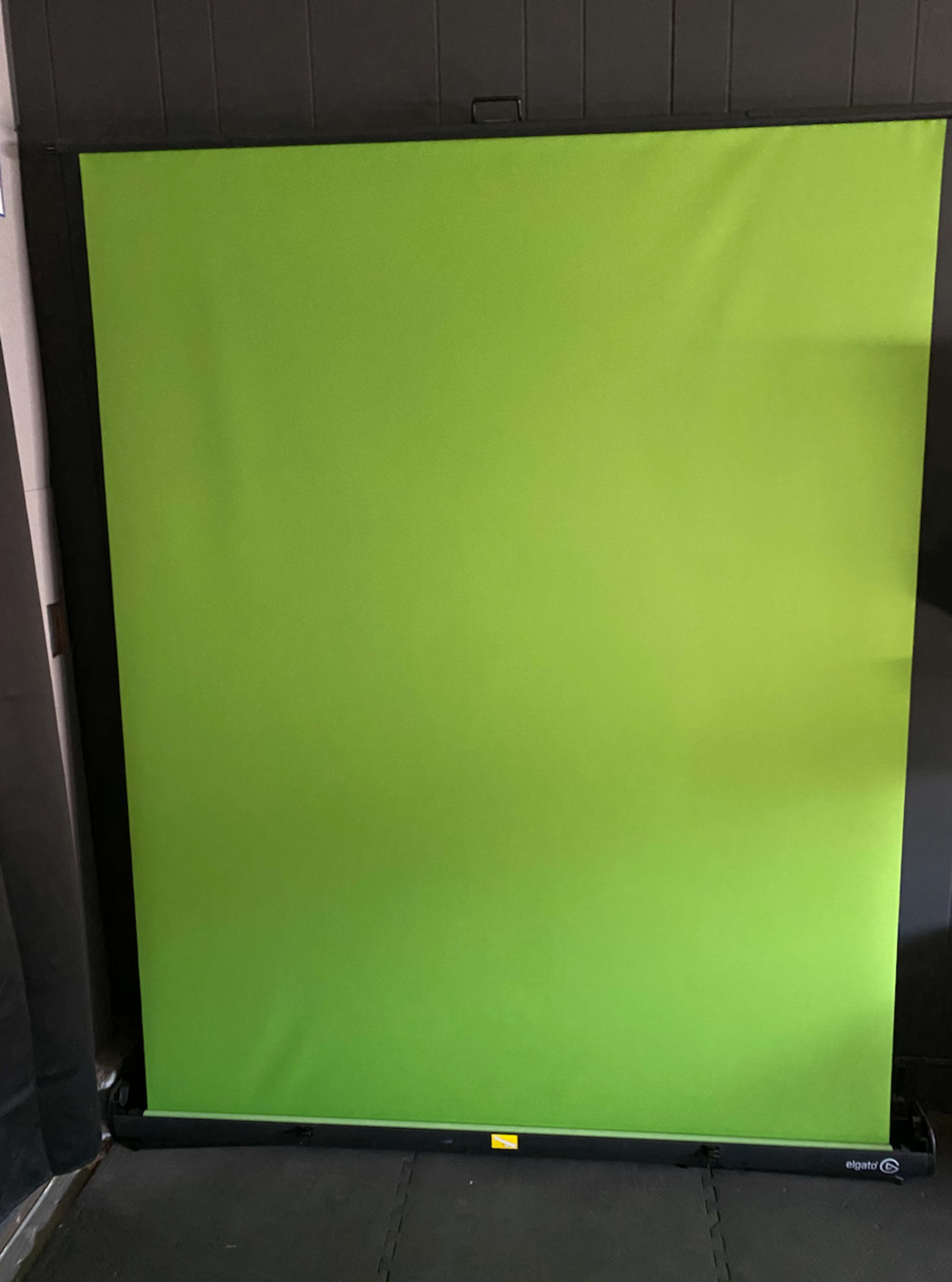 A green backdrop set up on a stand, positioned against a dark wall.