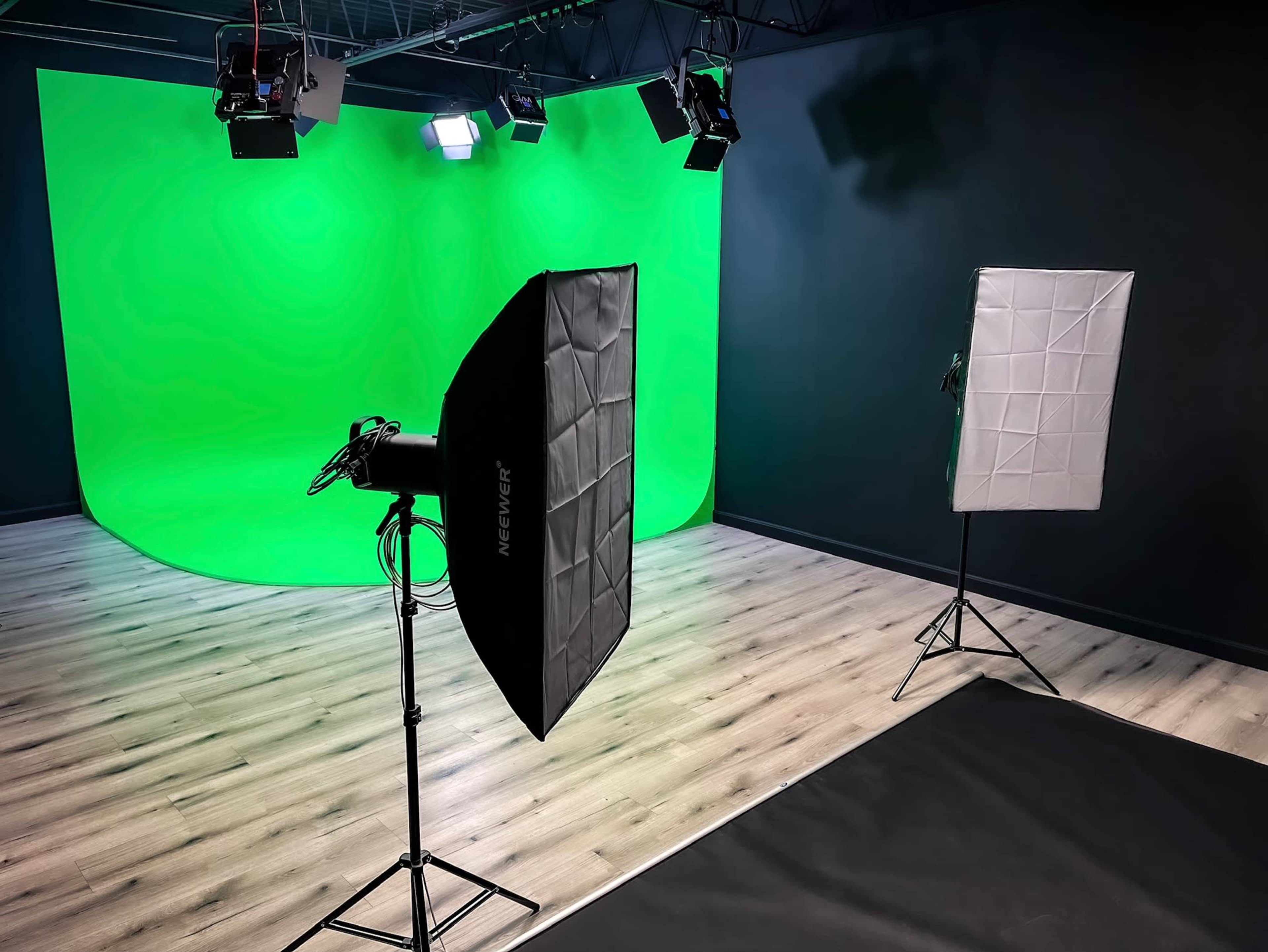A photography studio setup featuring a green backdrop, multiple lights, and softboxes positioned on the floor.